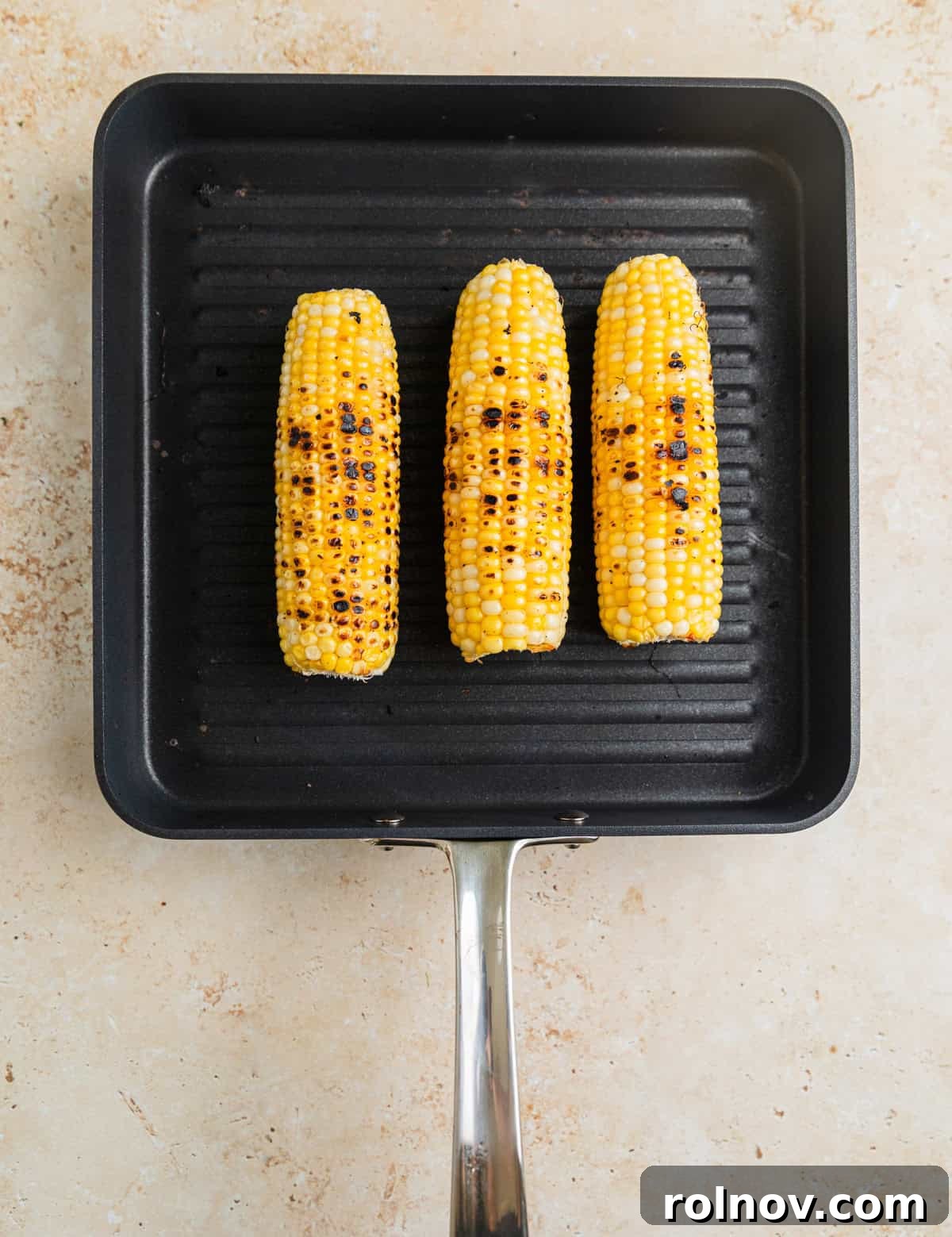 Charred Zucchini Pasta Toss 6 Two cobs of corn grilling on a grill pan with visible charring, suggesting a smoky and sweet flavor.