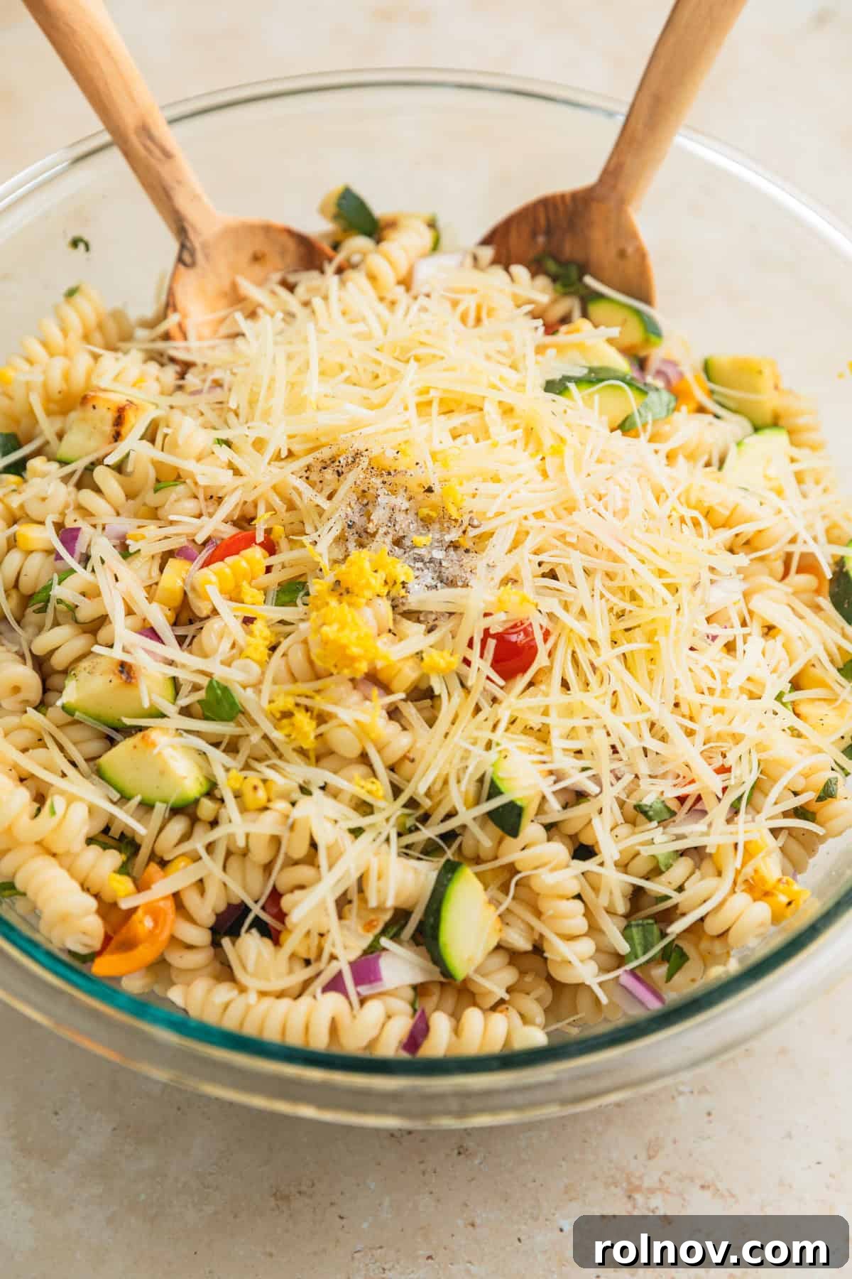 Charred Zucchini Pasta Toss 8 A bowl of tossed zucchini pasta salad, garnished with shredded Parmesan cheese, a drizzle of olive oil, and fresh lemon zest, showing off its fresh ingredients.