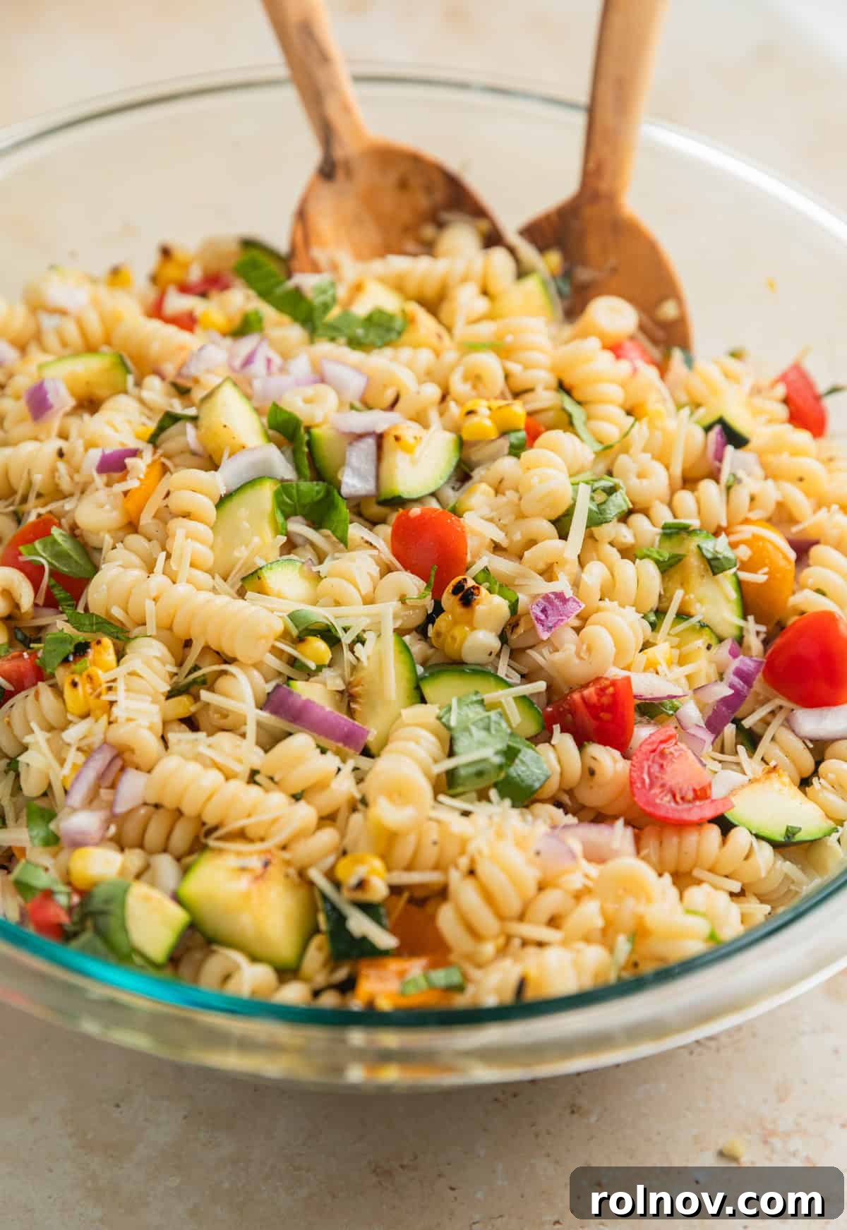 Charred Zucchini Pasta Toss 9 Tossed grilled vegetable pasta salad in a clear glass mixing bowl, with all ingredients evenly distributed and glistening with dressing.