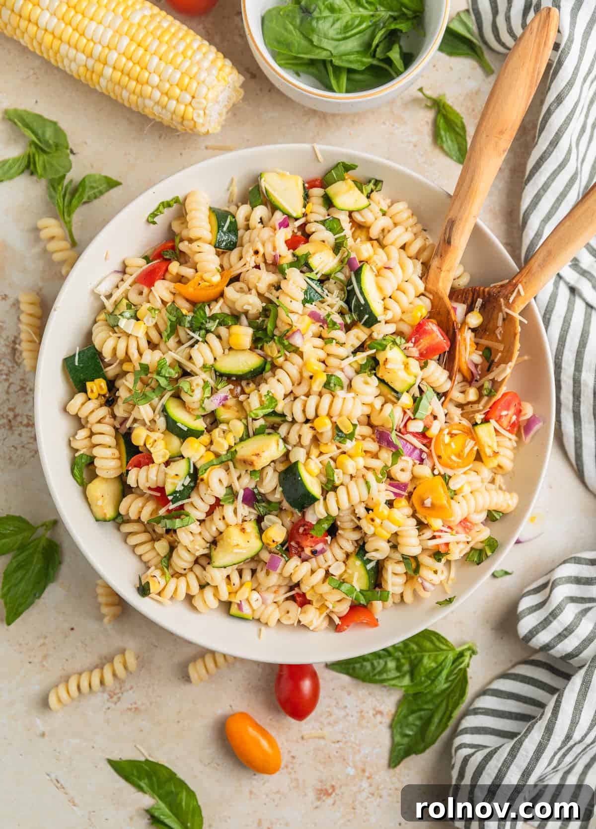 Charred Zucchini Pasta Toss 10 Overhead view of a large, colorful summer pasta salad in a serving bowl with two wooden serving spoons, ready to be enjoyed.