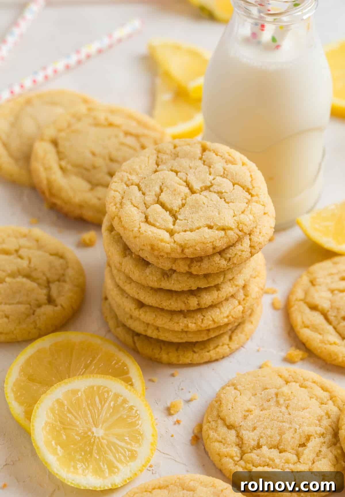 Bright Lemon Sugar Cookies 8 Lemon sugar cookies stacked on top of each other with glass of milk behind and other cookies and lemons surrounding.