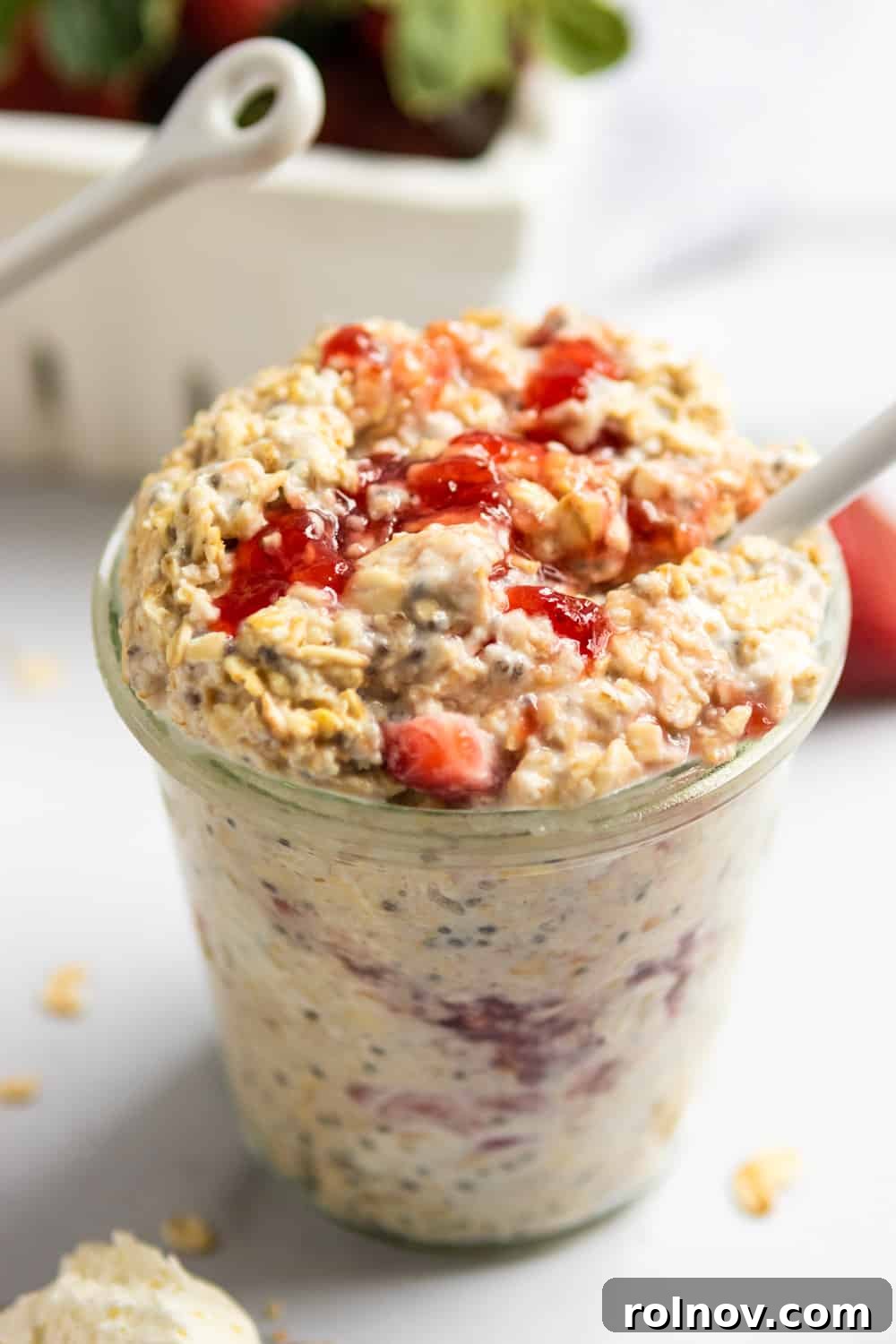 Decadent Strawberry Cheesecake Overnight Oats 2 Jar of strawberry cheesecake overnight oatmeal with white spoon and oats on counter surrounding.