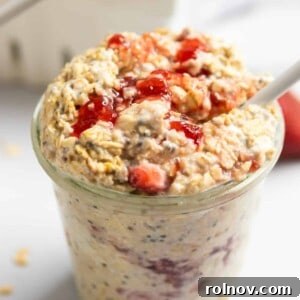 Decadent Strawberry Cheesecake Overnight Oats 5 Jar of strawberry cheesecake overnight oatmeal with white spoon and oats on counter surrounding.