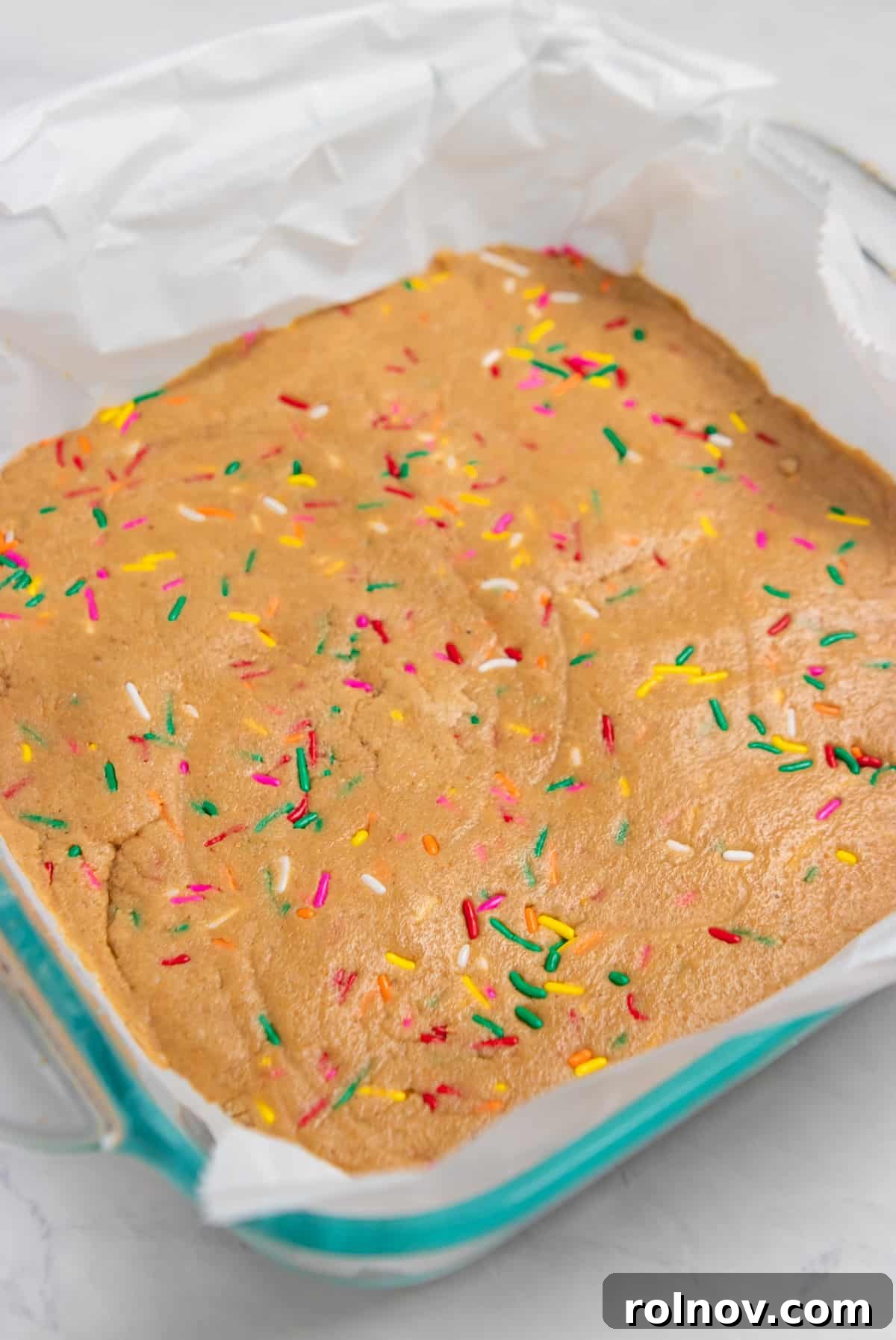 Birthday Cake Protein Bliss 6 Baking pan with no bake bars and rainbow sprinkles lined with parchment.