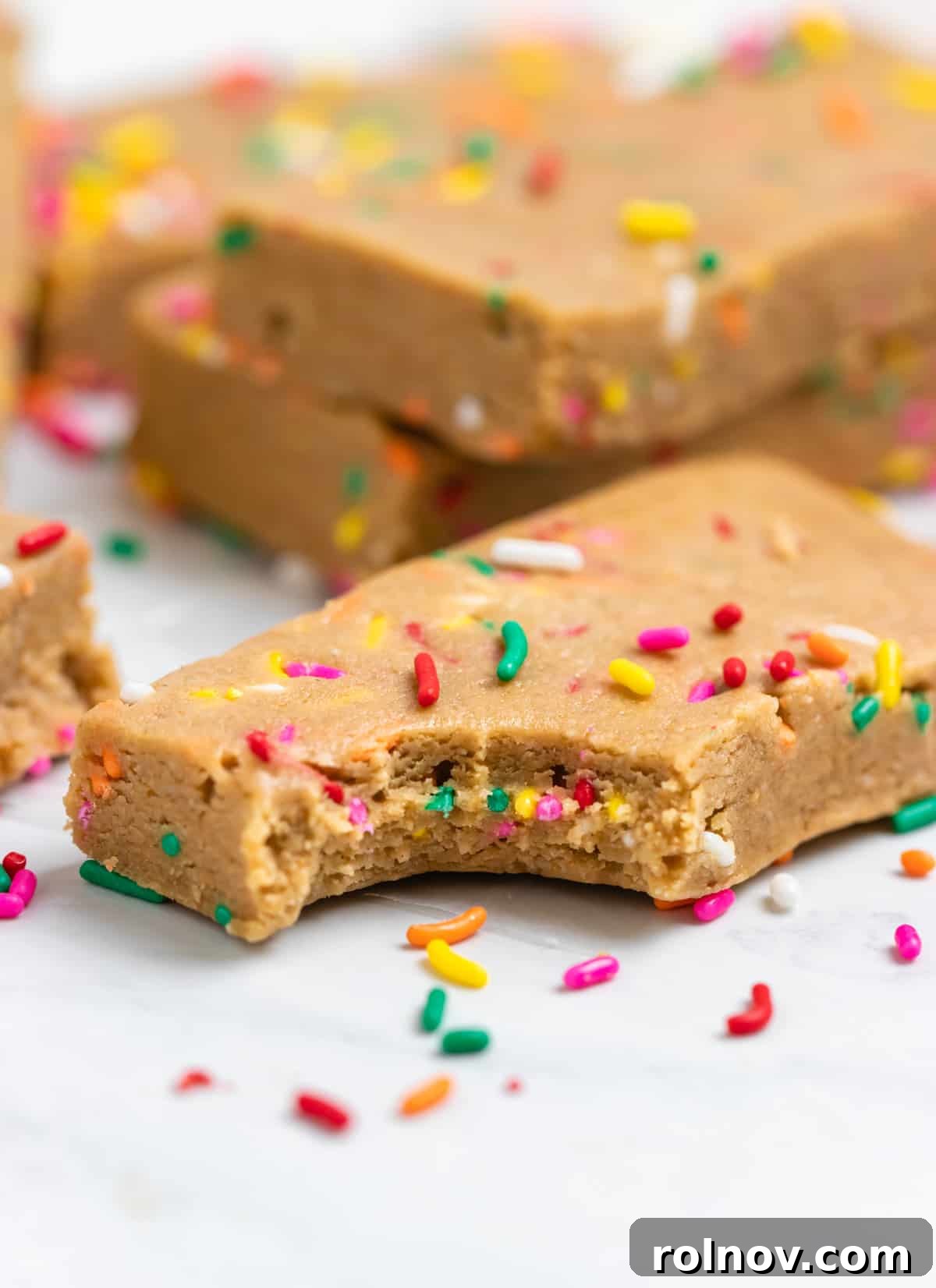 Birthday Cake Protein Bliss 7 Bite shot of protein bar on counter with rainbow sprinkles.