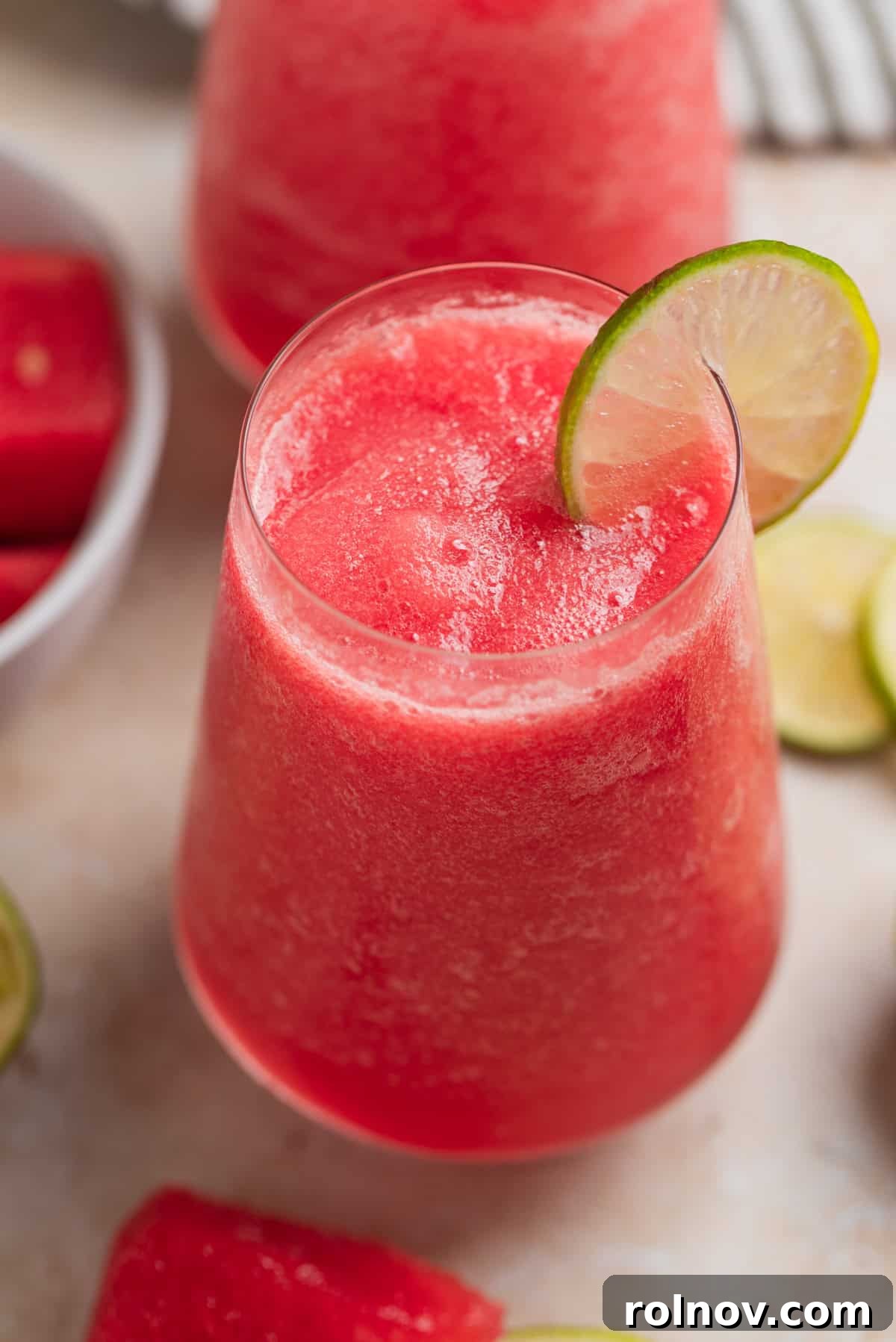 Blushing Watermelon Chill 2 Watermelon frose in glasses with lime slice and watermelon slices beside the glasses.