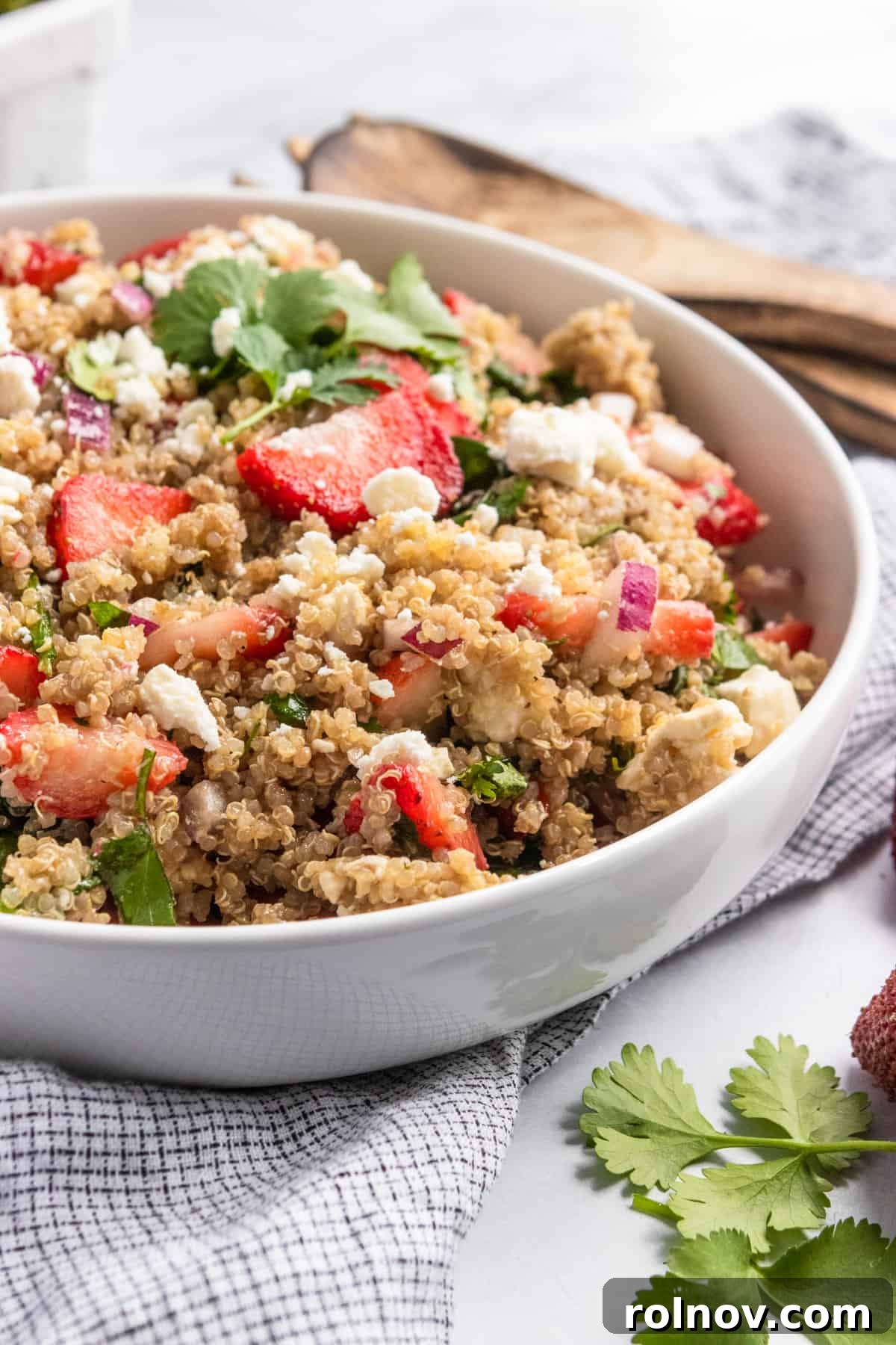 Refreshing Summer Strawberry Quinoa 2 Strawberry summer quinoa salad in white bowl with serving utensils, garnished with fresh mint.