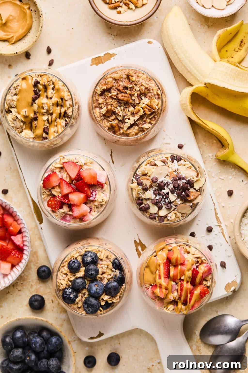 6 Simple Overnight Oats to Master Your Mornings 3 Oatmeal prepared in glasses on white cutting board and topped with berries, chocolate chips, peanut butter, etc.