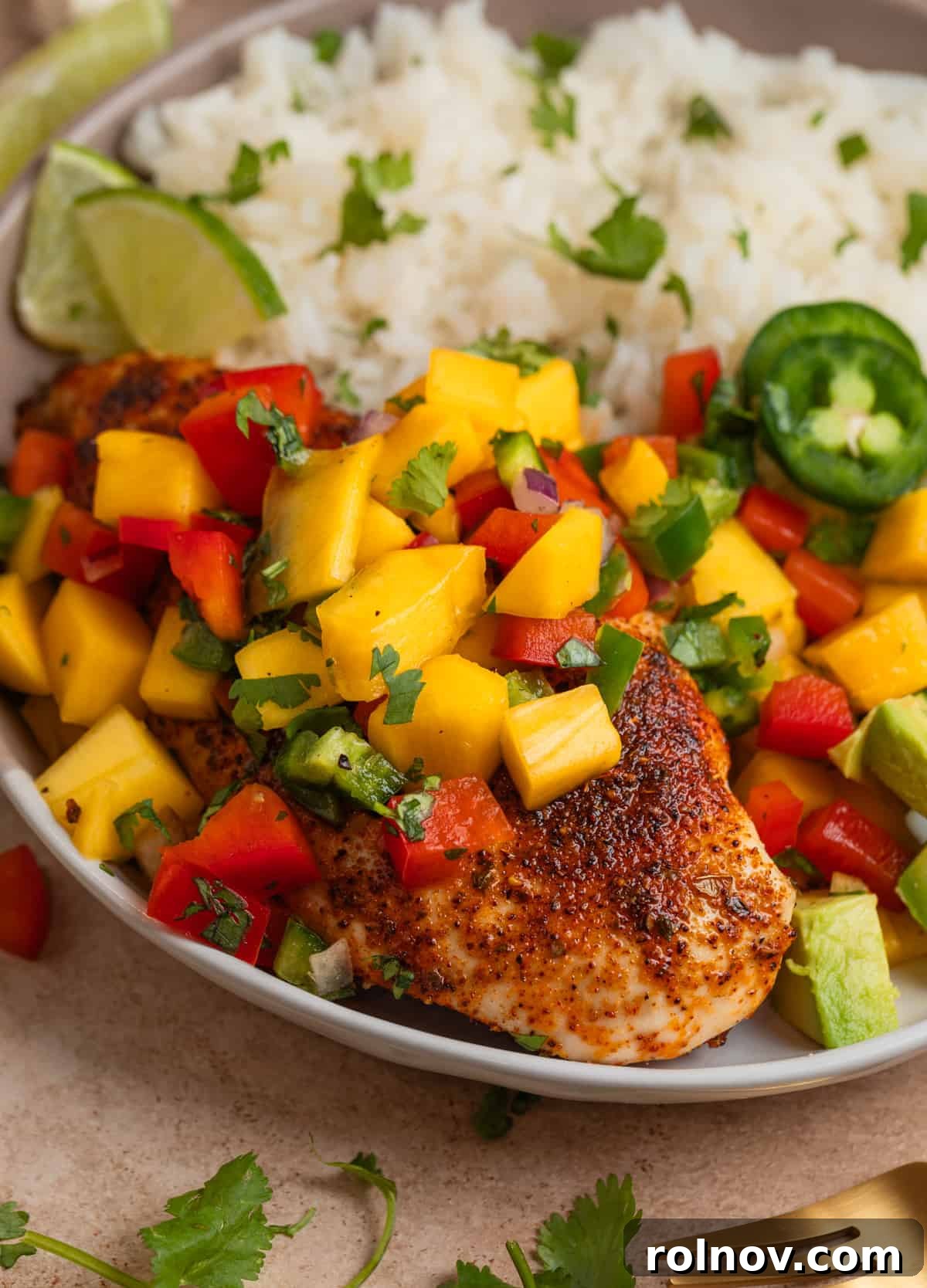 Tropical Mango Chicken 2 Baked chicken with a rich spice rub, generously topped with refreshing mango salsa and garnished with fresh cilantro, ready to be served.