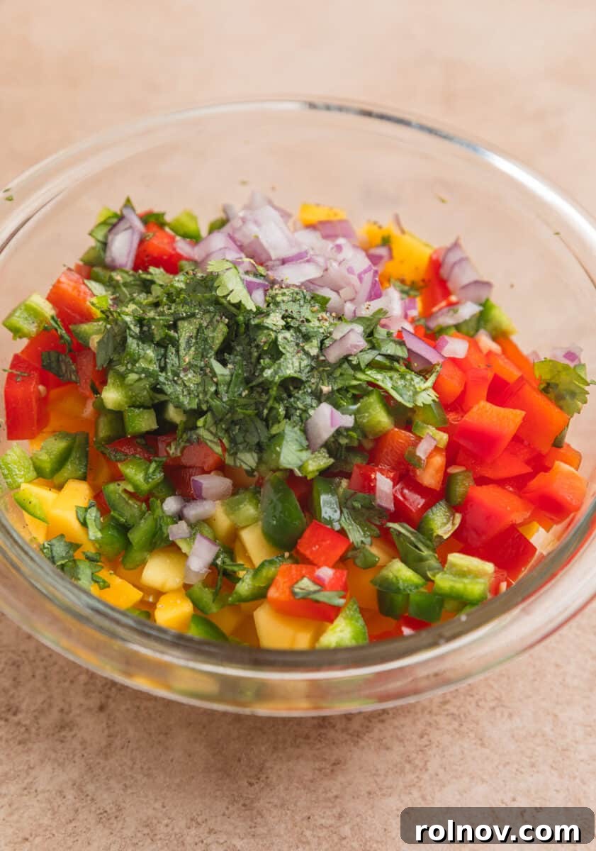 Tropical Mango Chicken 6 A mixing bowl filled with freshly diced mango, red bell pepper, red onion, jalapeño, and other vibrant salsa ingredients, ready to be combined.