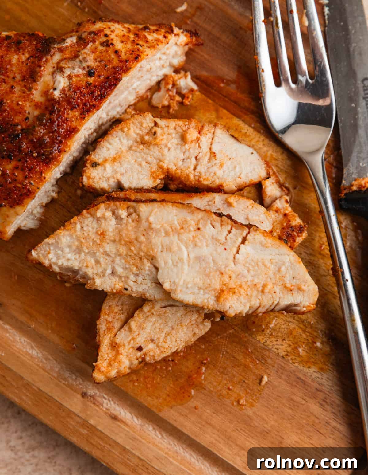 Tropical Mango Chicken 8 Perfectly sliced chicken breast arranged on a cutting board, accompanied by a fork and knife, showcasing its tender, juicy interior.