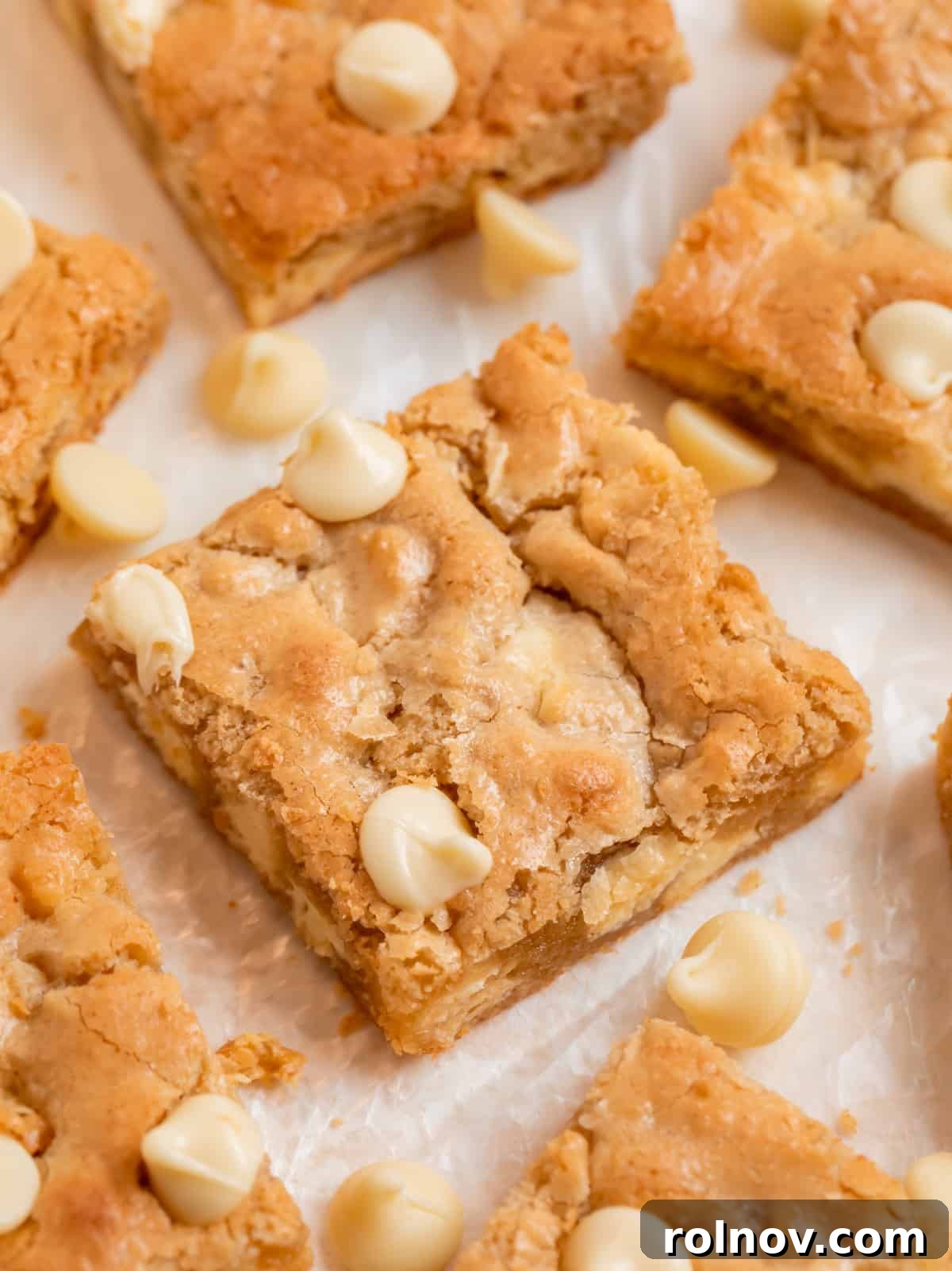 Close-up of golden almond flour blondies, generously studded with white chocolate chips and arranged on wax paper.