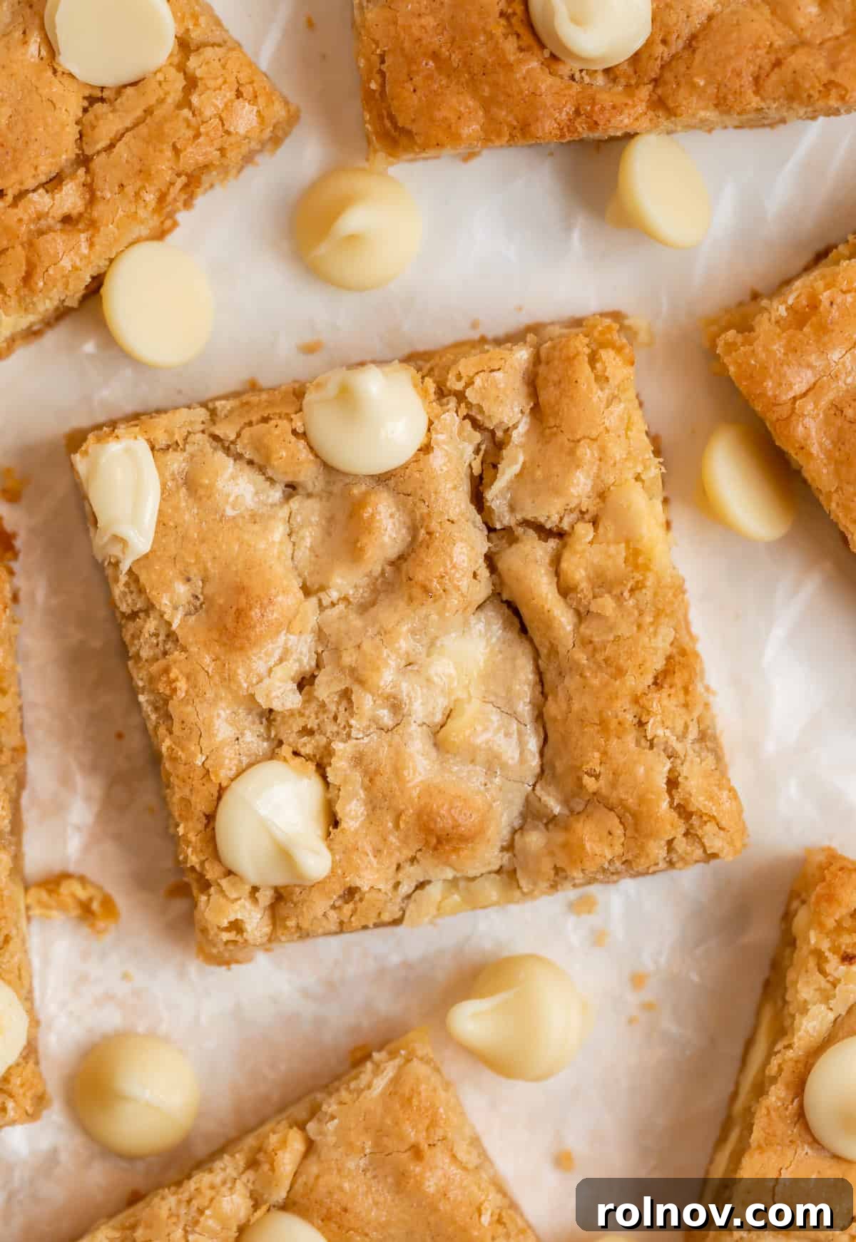 Gluten-free white chocolate chip blondies meticulously arranged on parchment paper, ready to be enjoyed.