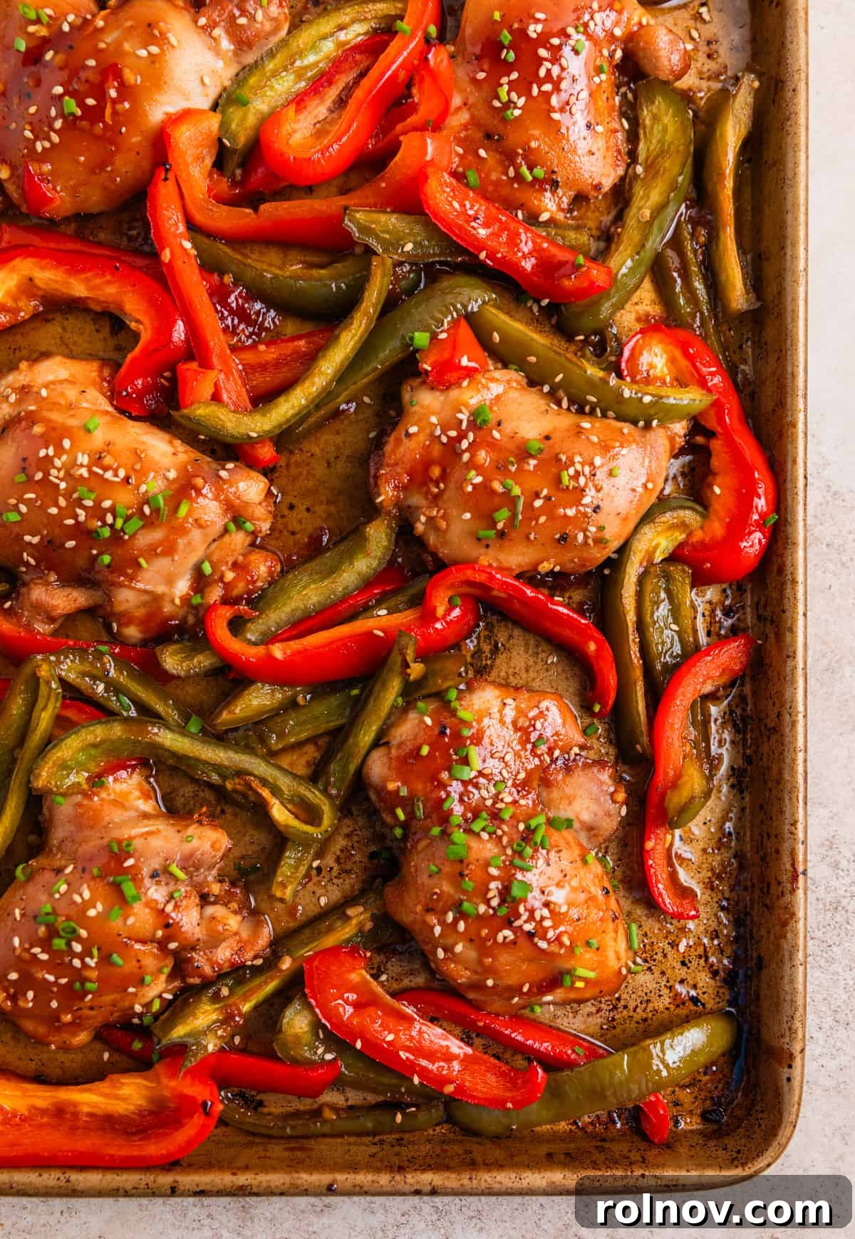 One-Pan Honey Garlic Chicken Thigh Dinner 2 Chicken thighs and red and green bell peppers baked on sheet pan and topped with chives and sesame seeds.