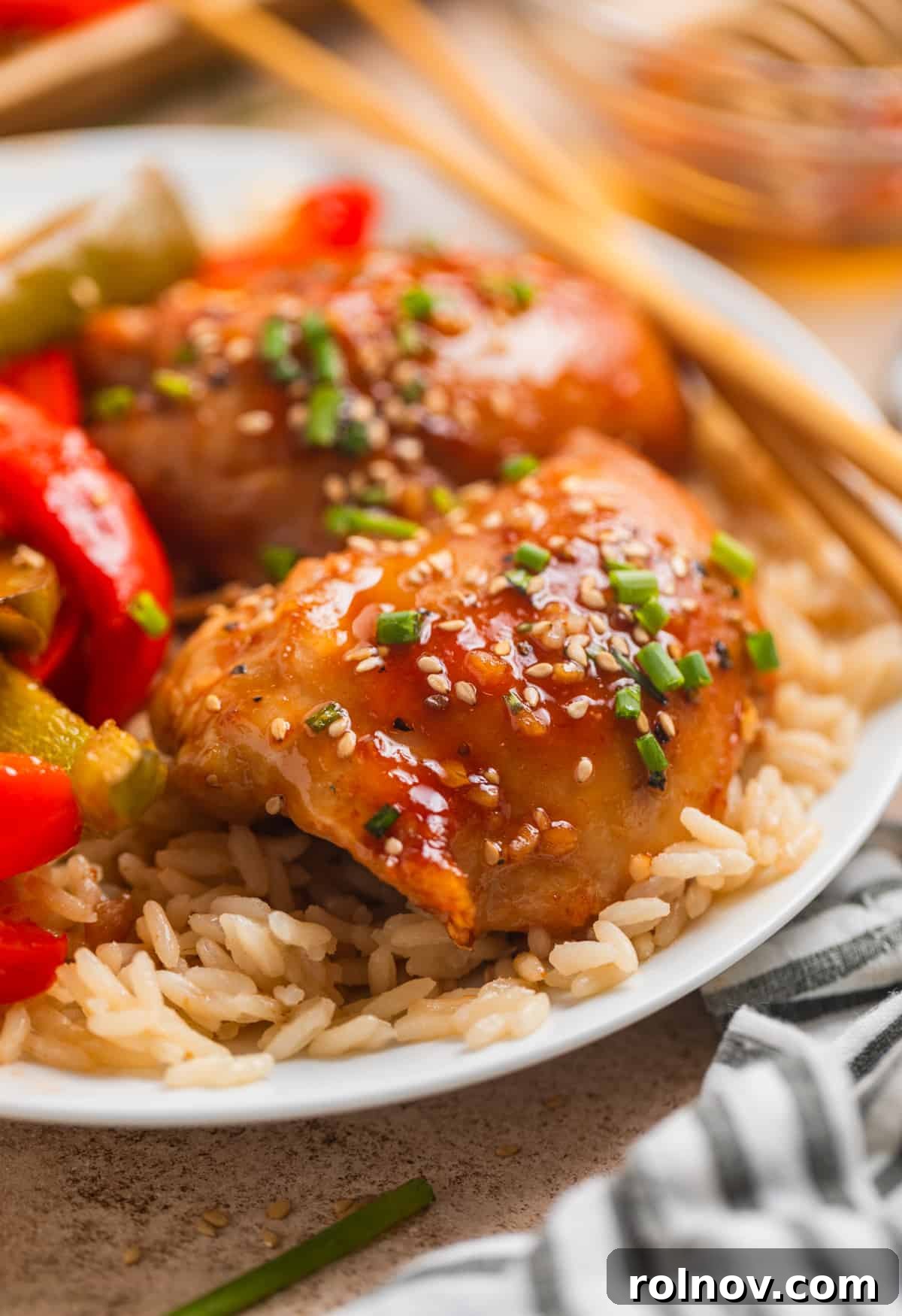 One-Pan Honey Garlic Chicken Thigh Dinner 3 Honey garlic chicken thighs with peppers over rice on white plate.