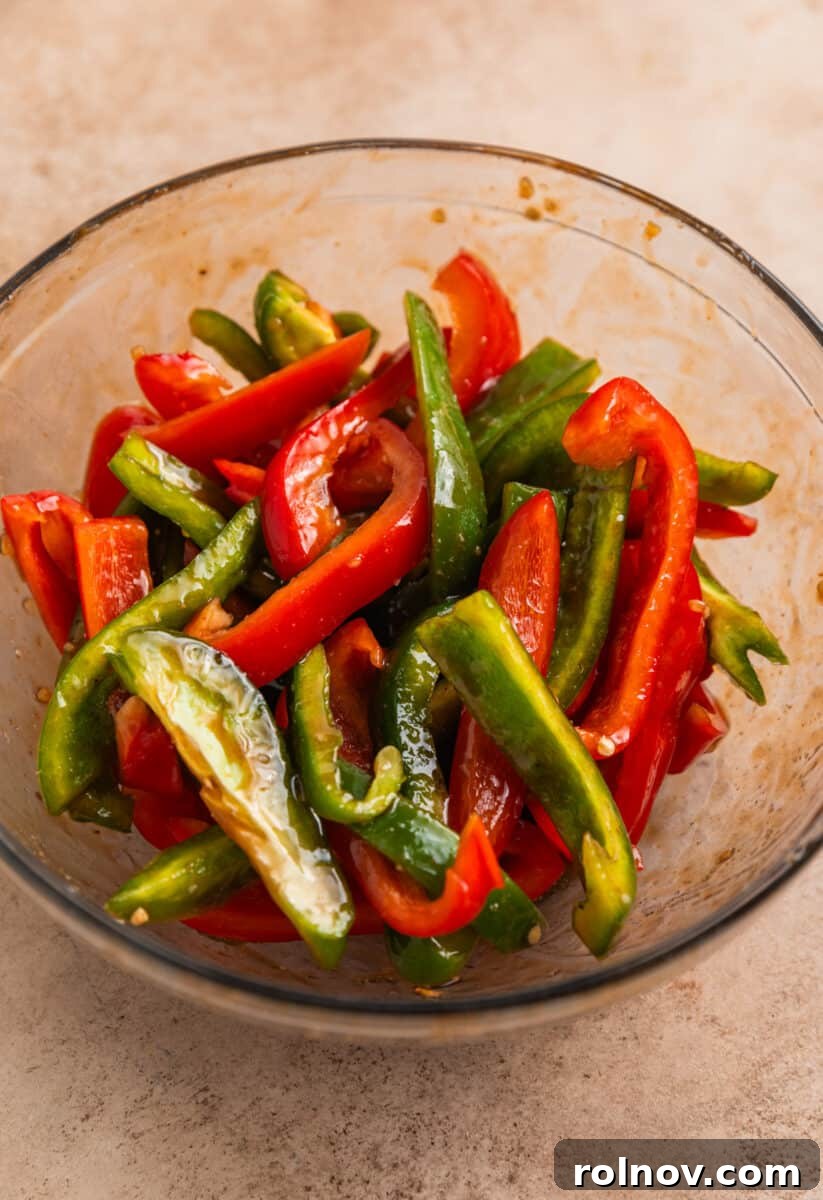 One-Pan Honey Garlic Chicken Thigh Dinner 7 Bell peppers tossed with sauce in glass mixing bowl.