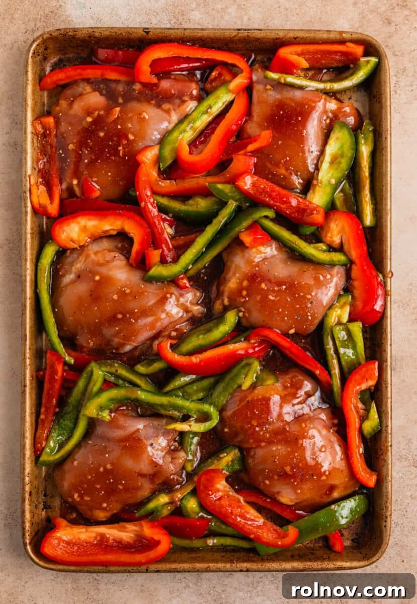 One-Pan Honey Garlic Chicken Thigh Dinner 8 Bell peppers and honey garlic sauce covered chicken thighs arranged on sheet pan before cooking.