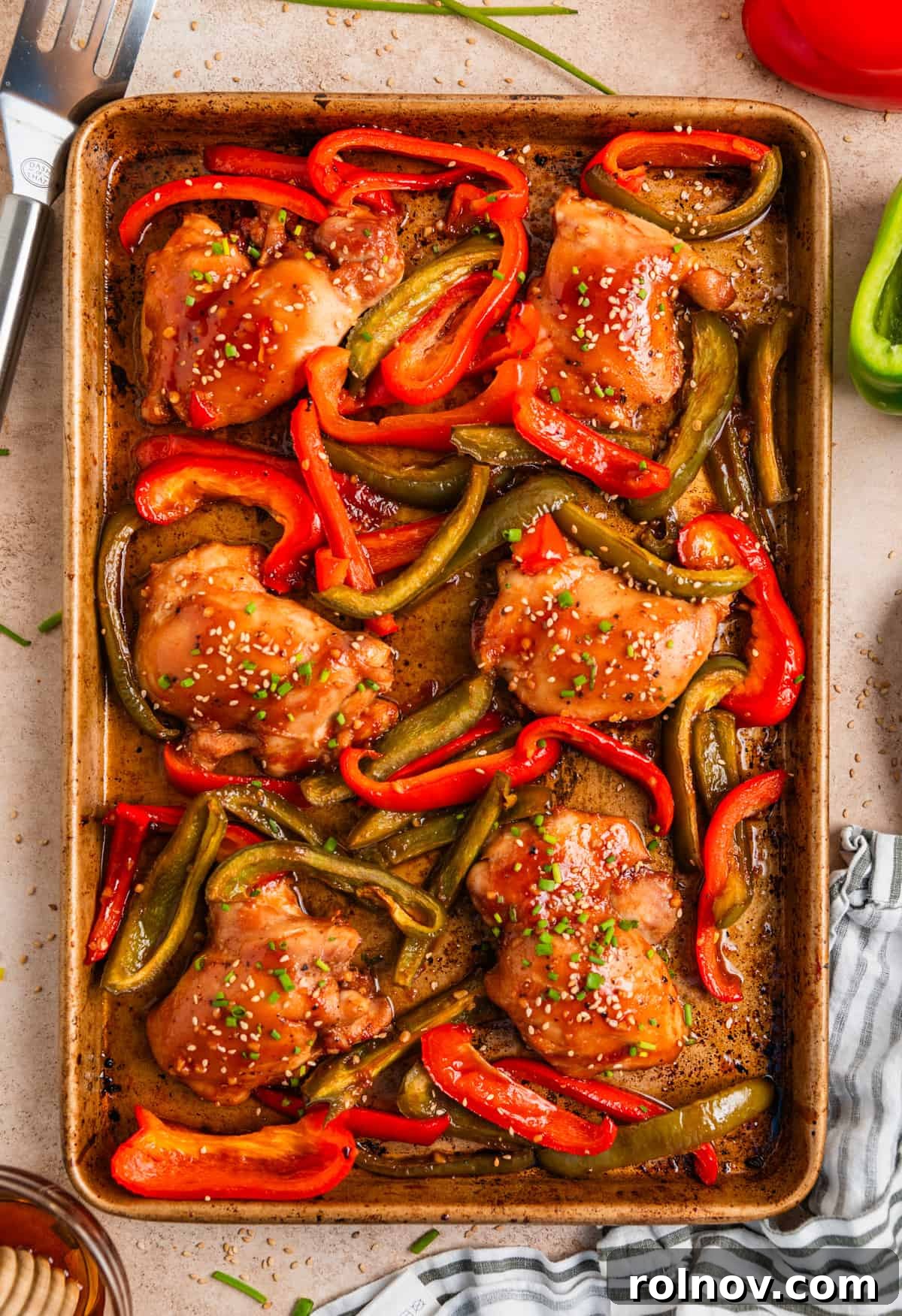 One-Pan Honey Garlic Chicken Thigh Dinner 9 Chicken thighs and bell peppers on cookie sheet topped with sesame seeds and chives.