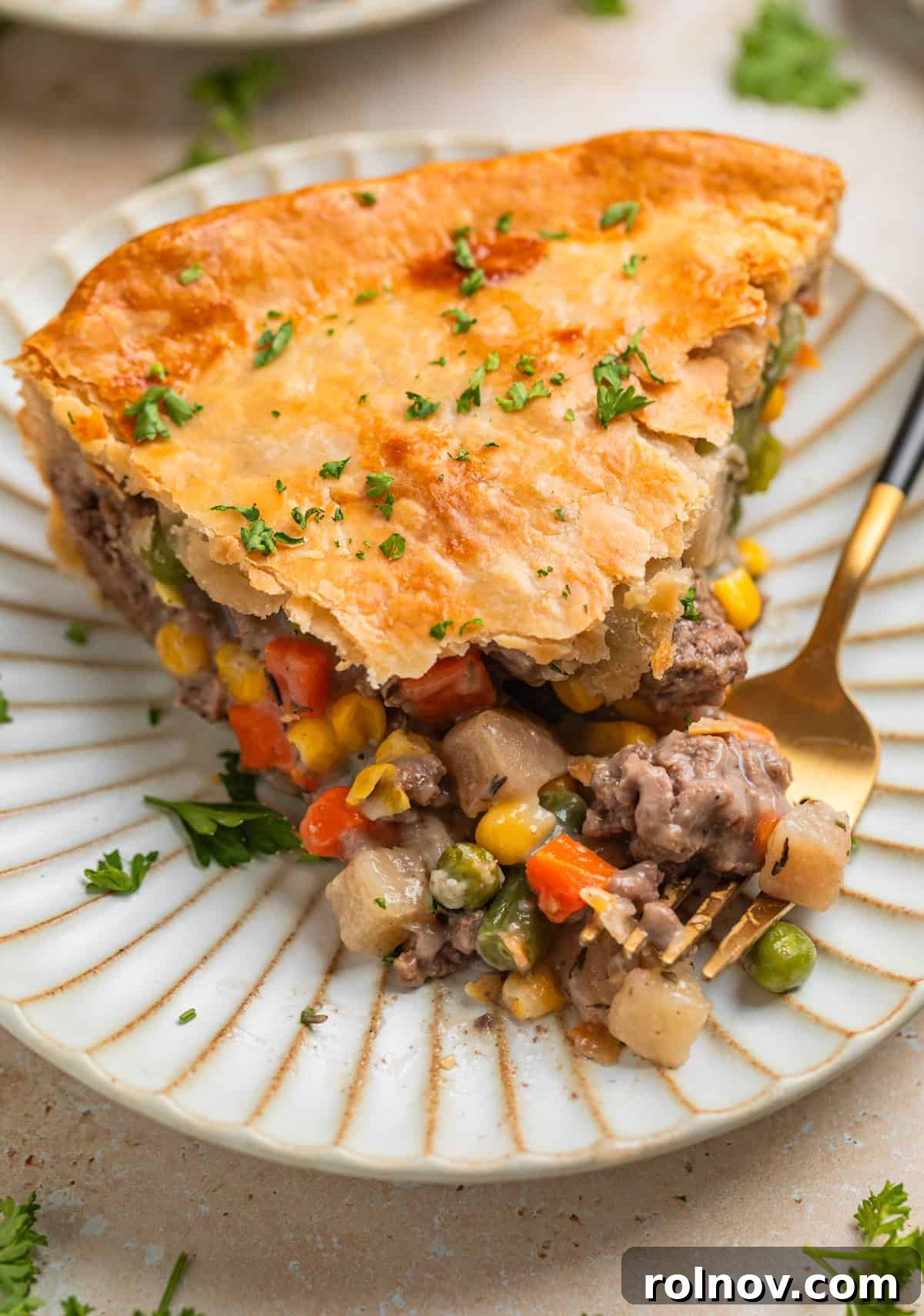 Hearty Beef Pot Pie 2 A generous slice of golden-crusted Ground Beef Pot Pie on a plate with a fork, showing the rich filling inside.