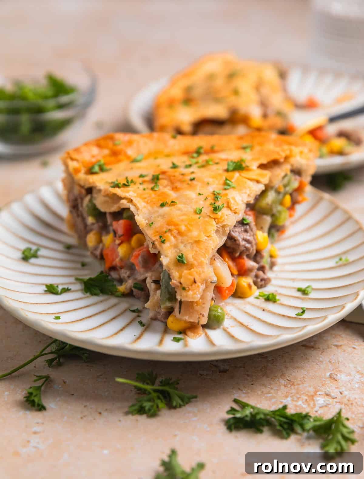 Hearty Beef Pot Pie 13 A perfectly portioned slice of ground beef pie on a white dish, topped with a sprinkle of fresh parsley, revealing its rich, creamy filling and golden, flaky crust.