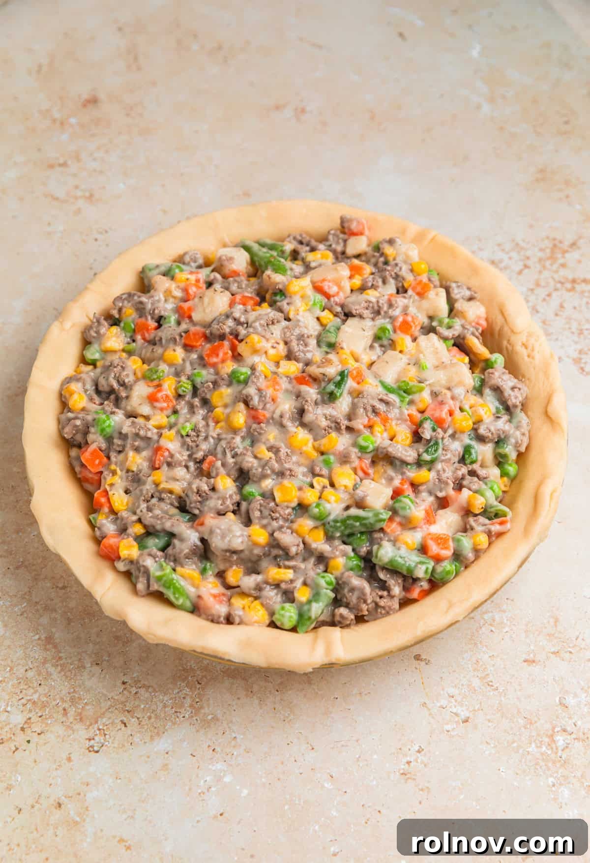 Hearty Beef Pot Pie 8 The rich ground beef and vegetable filling evenly distributed over the bottom pie crust in a pie dish, ready for the top crust.