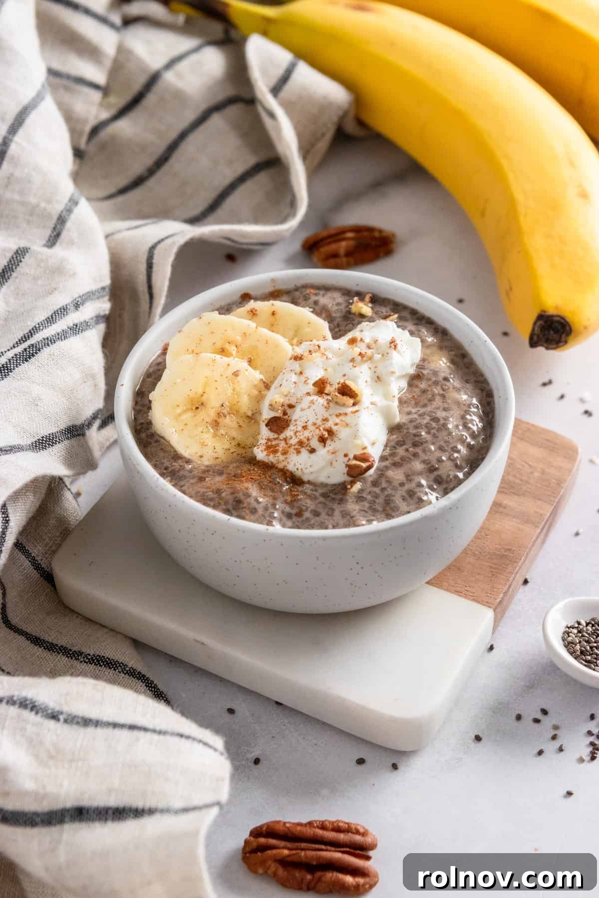 Wholesome Banana Chia Seed Pudding 6 Chia pudding in bowl on coaster with bananas and pecans in the background.