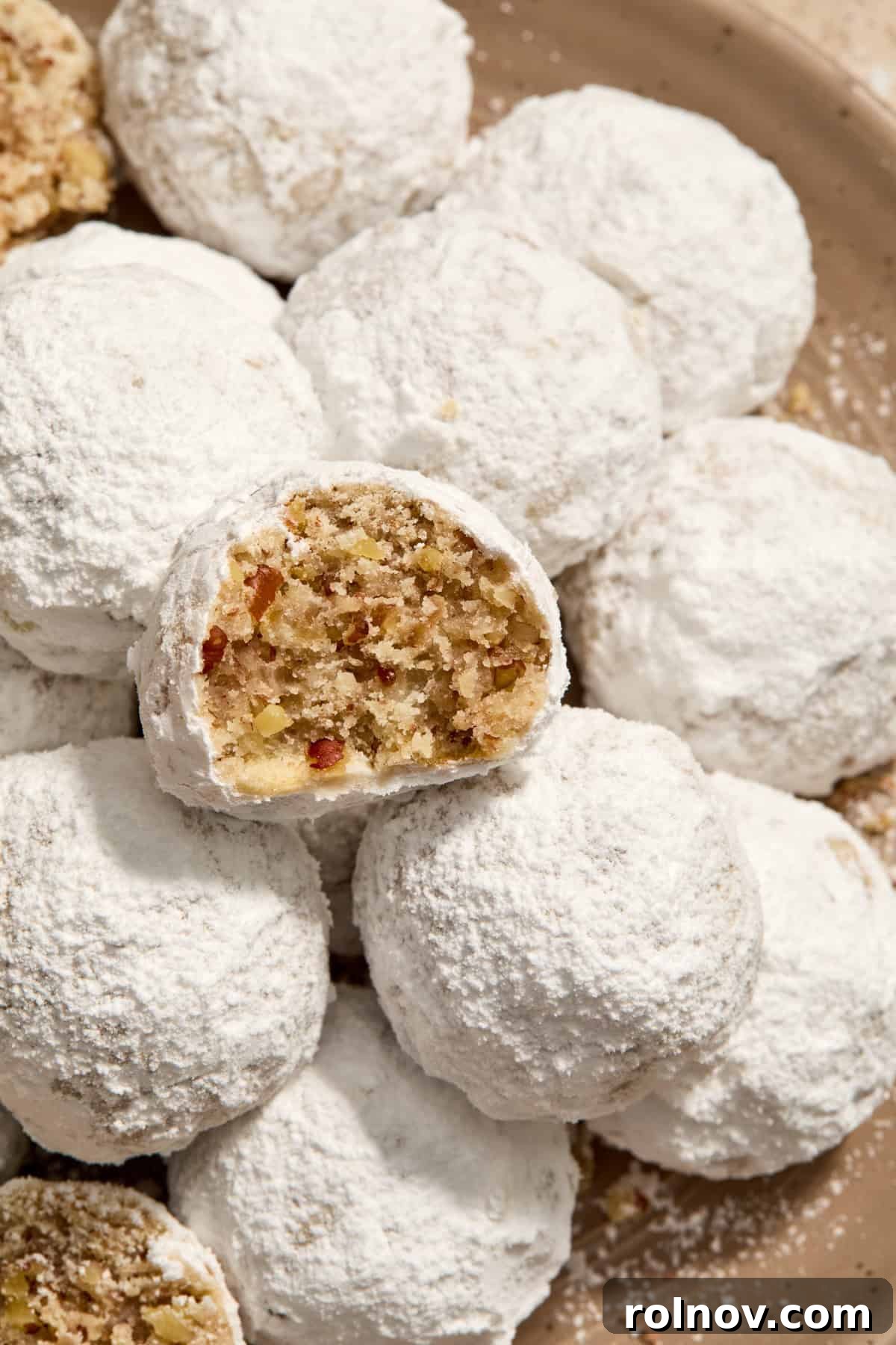 Velvety Pecan Cream Cheese Snowflakes 2 Cream cheese Christmas cookies with pecans and covered in powdered sugar on plate with bite taken out of one cookie.