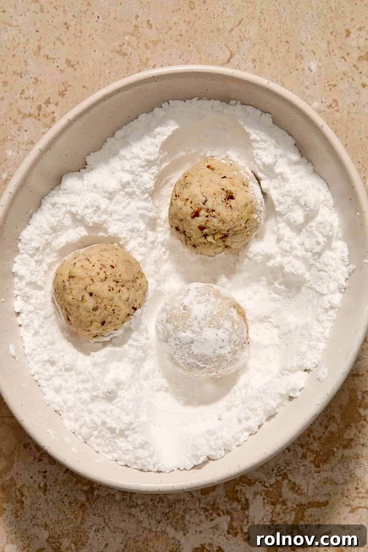 Velvety Pecan Cream Cheese Snowflakes 13 Snowball cookies rolled in powdered sugar in bowl.