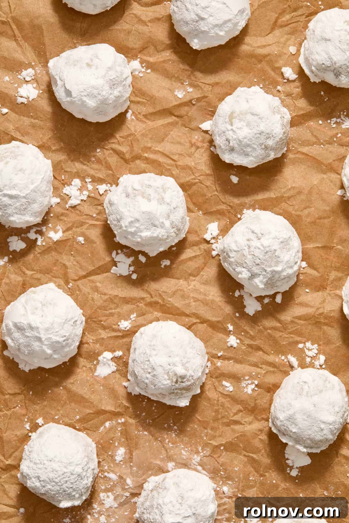 Velvety Pecan Cream Cheese Snowflakes 14 Parchment paper with powdered sugar covered cookies arranged.