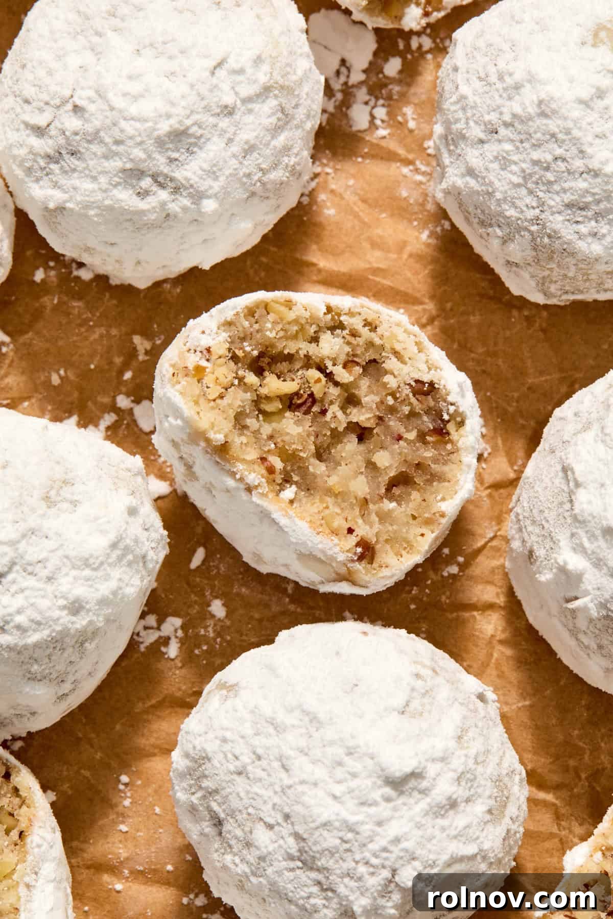 Velvety Pecan Cream Cheese Snowflakes 3 Parchment paper with pecan snowball cookies arranged on top and bite taken from one cookie.