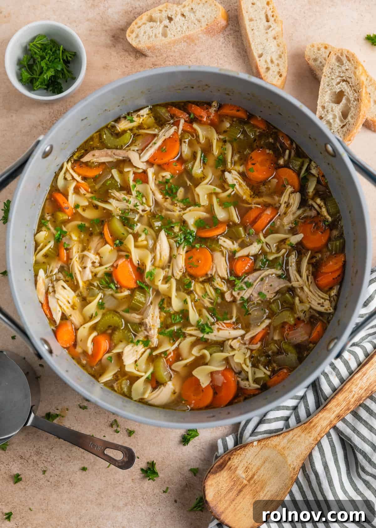 Shortcut Rotisserie Chicken Noodle Soup 3 A large pot of steaming chicken noodle soup, surrounded by fresh bread slices and a sprinkle of parsley, inviting a warm meal.