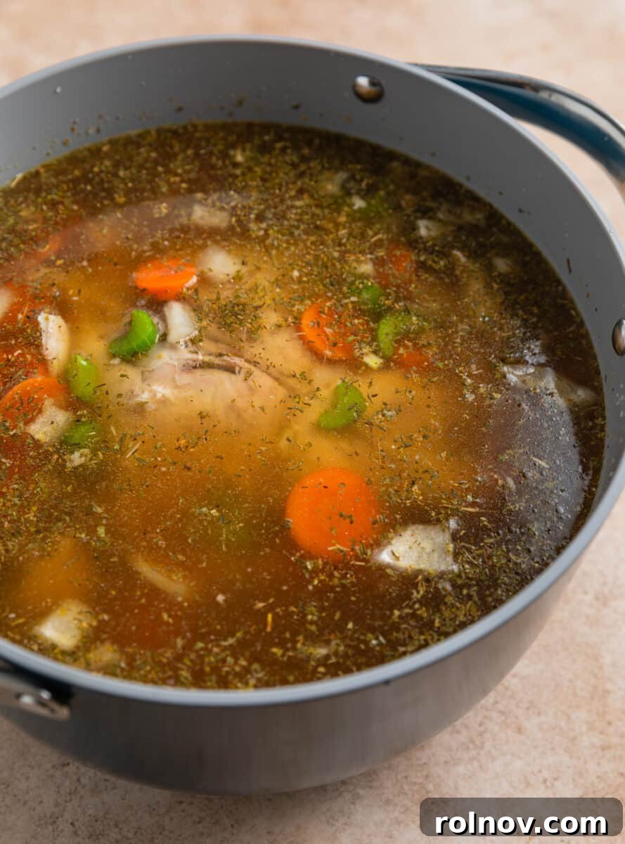 Shortcut Rotisserie Chicken Noodle Soup 7 Rich chicken broth being poured over the soup ingredients in the pot, beginning the simmering process.