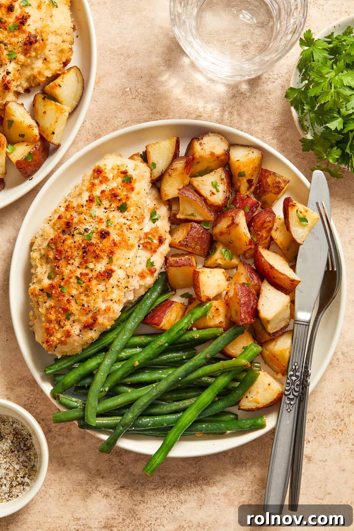 Golden Parmesan Chicken Sheet Pan Feast 3 Parmesan baked chicken, roasted potatoes and green beans on white plate with fork and knife.