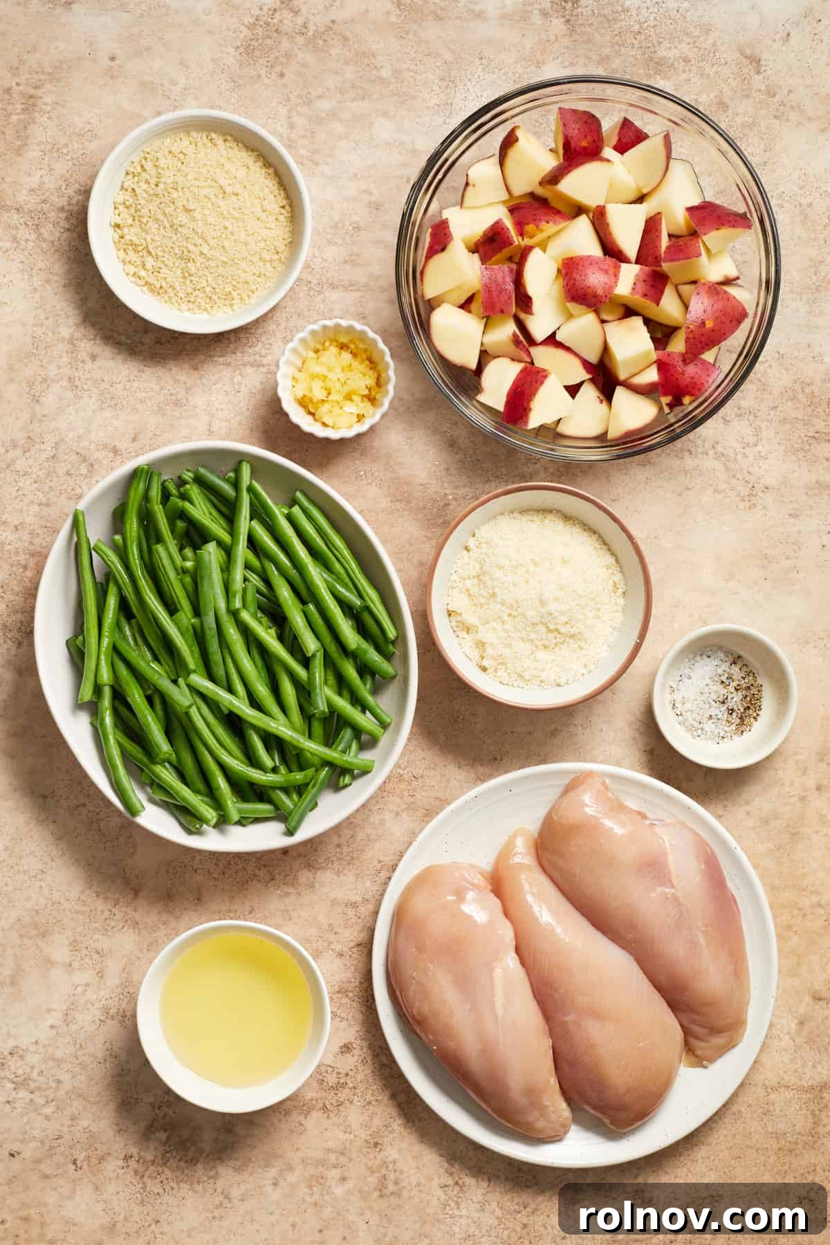 Golden Parmesan Chicken Sheet Pan Feast 4 Chicken breast, green beans, potatoes, olive oil, parmesan and other ingredients needed for recipe on surface.