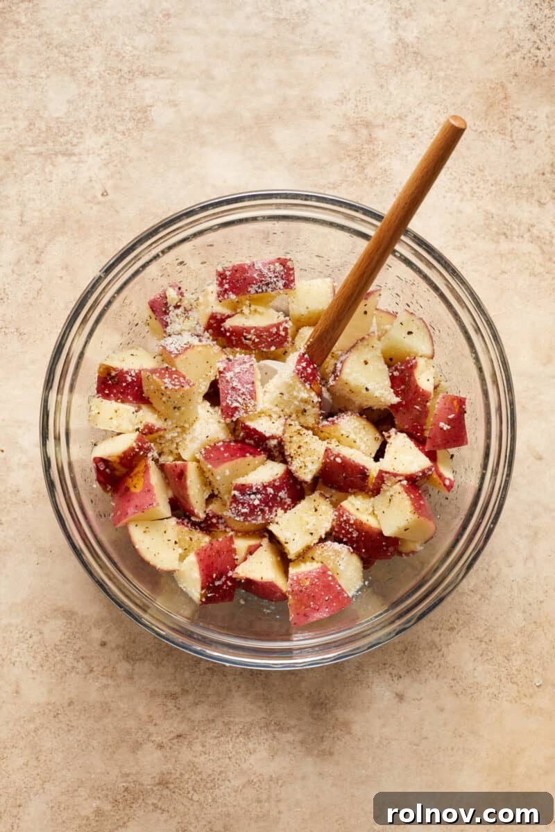 Golden Parmesan Chicken Sheet Pan Feast 5 Quartered red potatoes in glass bowl with seasoning and parmesan and spatula.