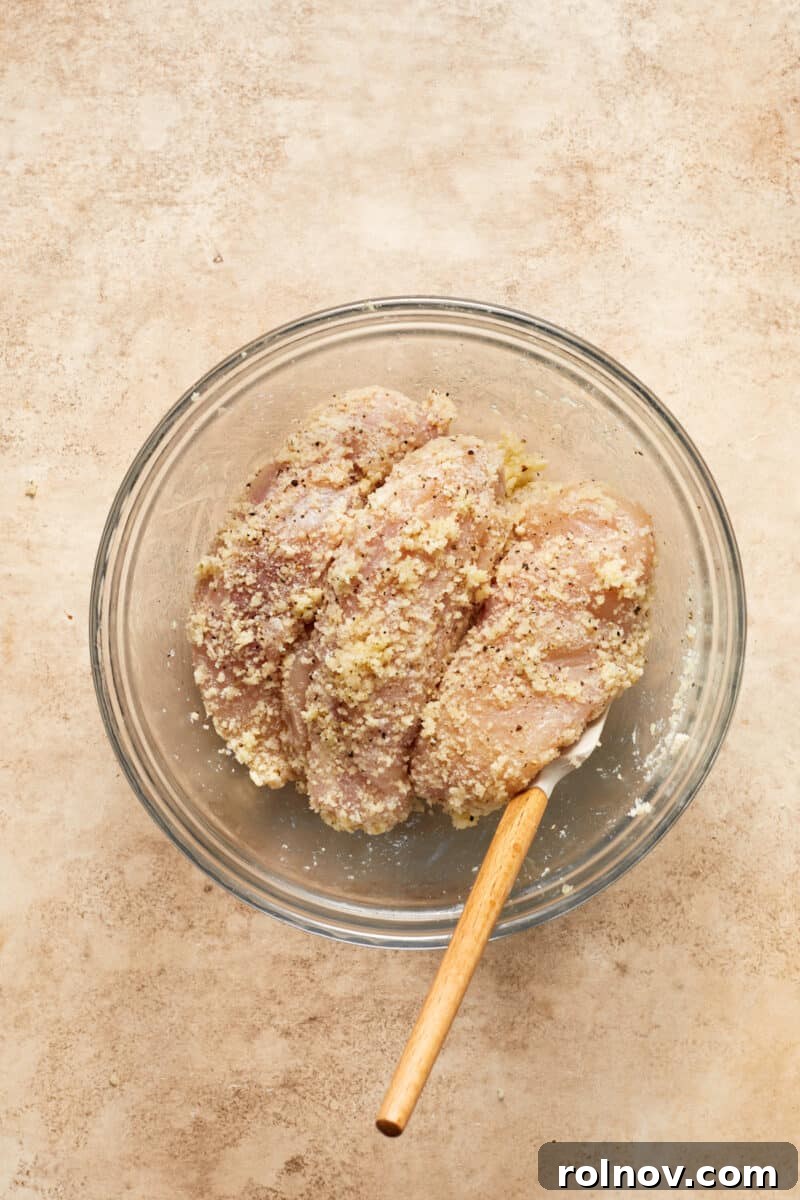 Golden Parmesan Chicken Sheet Pan Feast 7 Chicken breast in glass mixing bowl tossed with parmesan, breadcrumbs and seasoning.