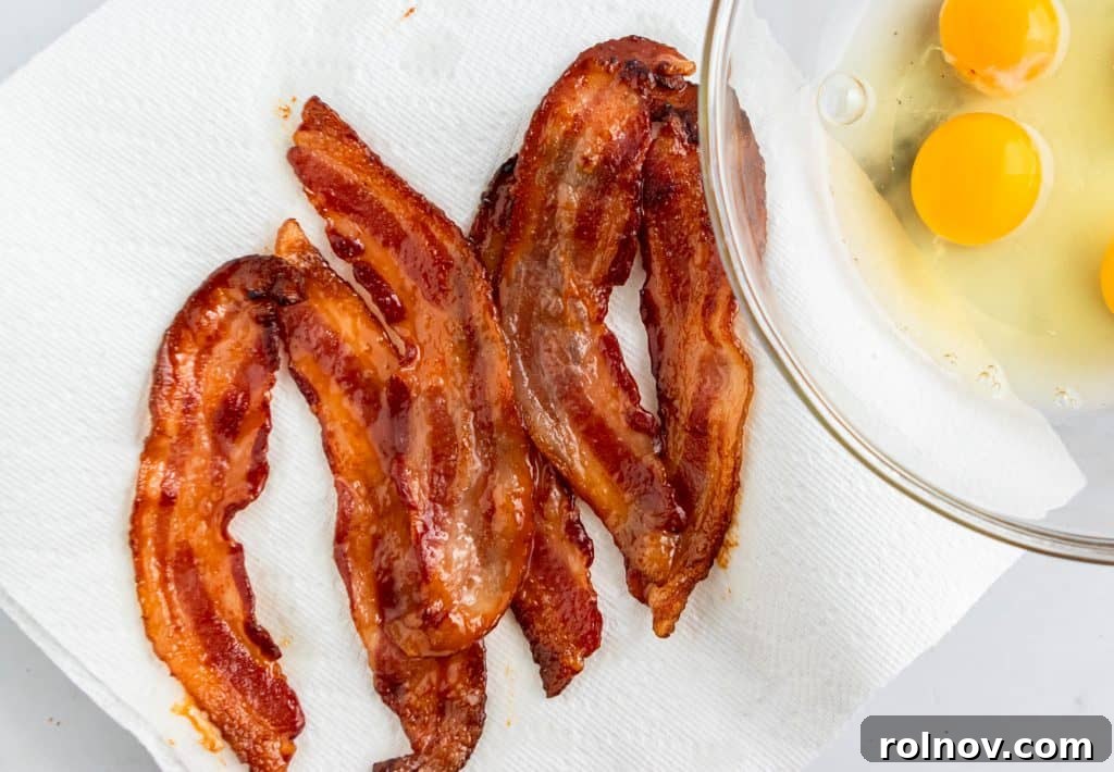 Crispy strips of maple-glazed bacon resting on a paper towel, showcasing their perfect texture and sweet-savory coating, ready to be incorporated into a dish.
