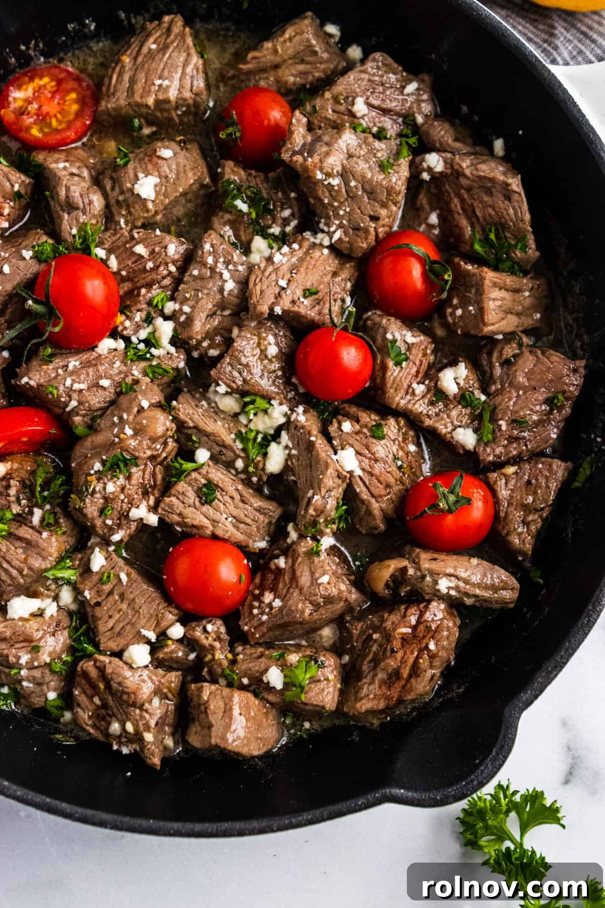 Steak bites in skillet with fresh tomatoes, feta and parsley.