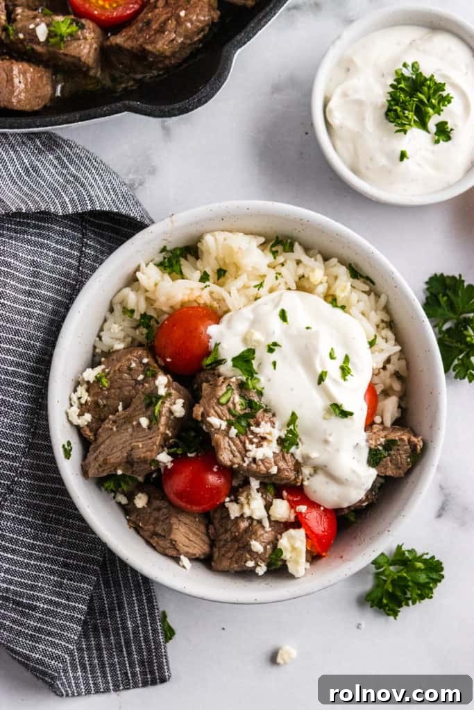 Overhead shot of bowl with steak bites, tomatoes, parsley, feta and yogurt sauce.