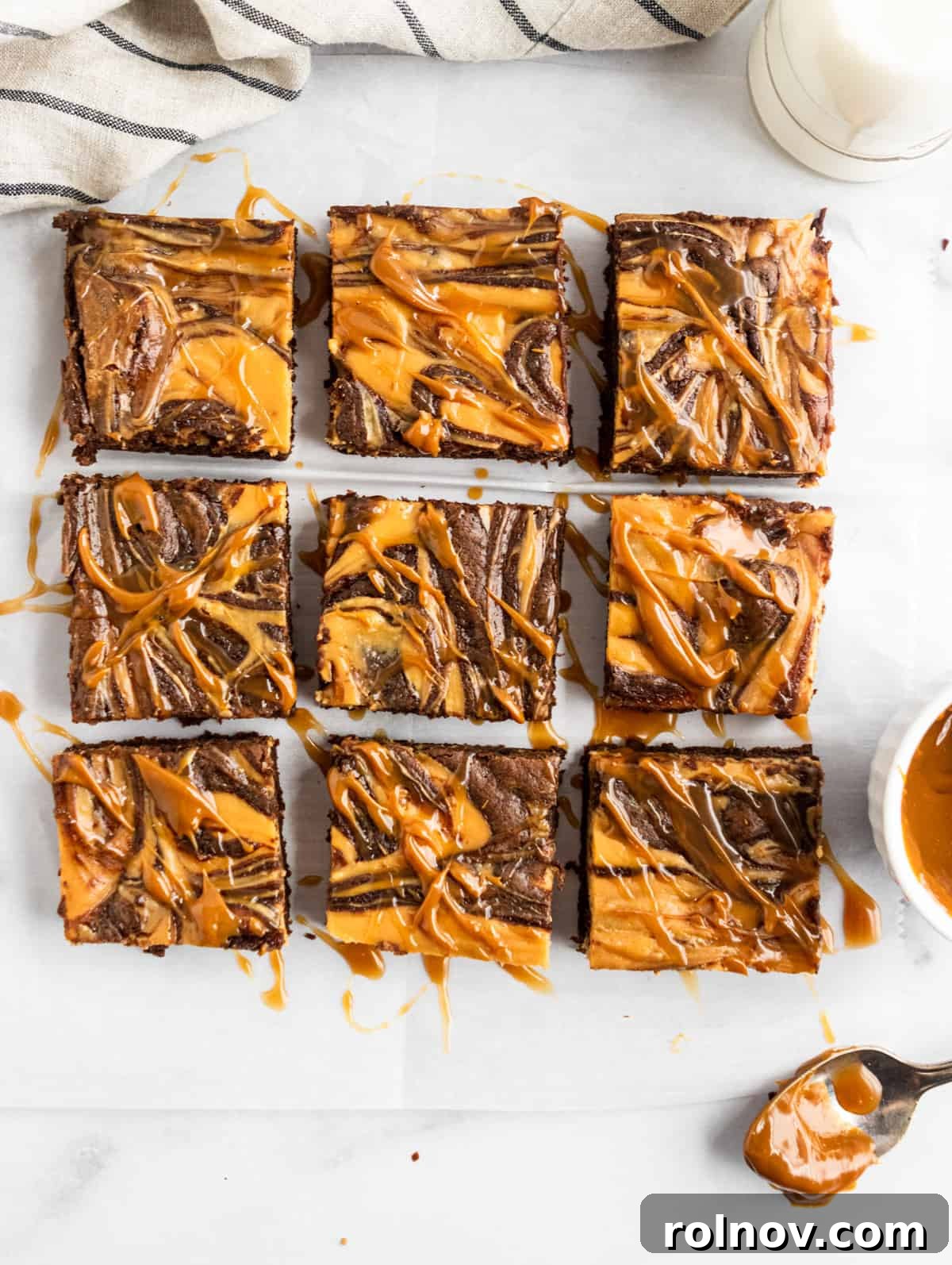 Overhead shot of sliced brownies with dulce de leche drizzle. Neatly cut squares of fudgy brownies, each showcasing a distinct dulce de leche cheesecake swirl and a glossy drizzle of extra dulce de leche on top.
