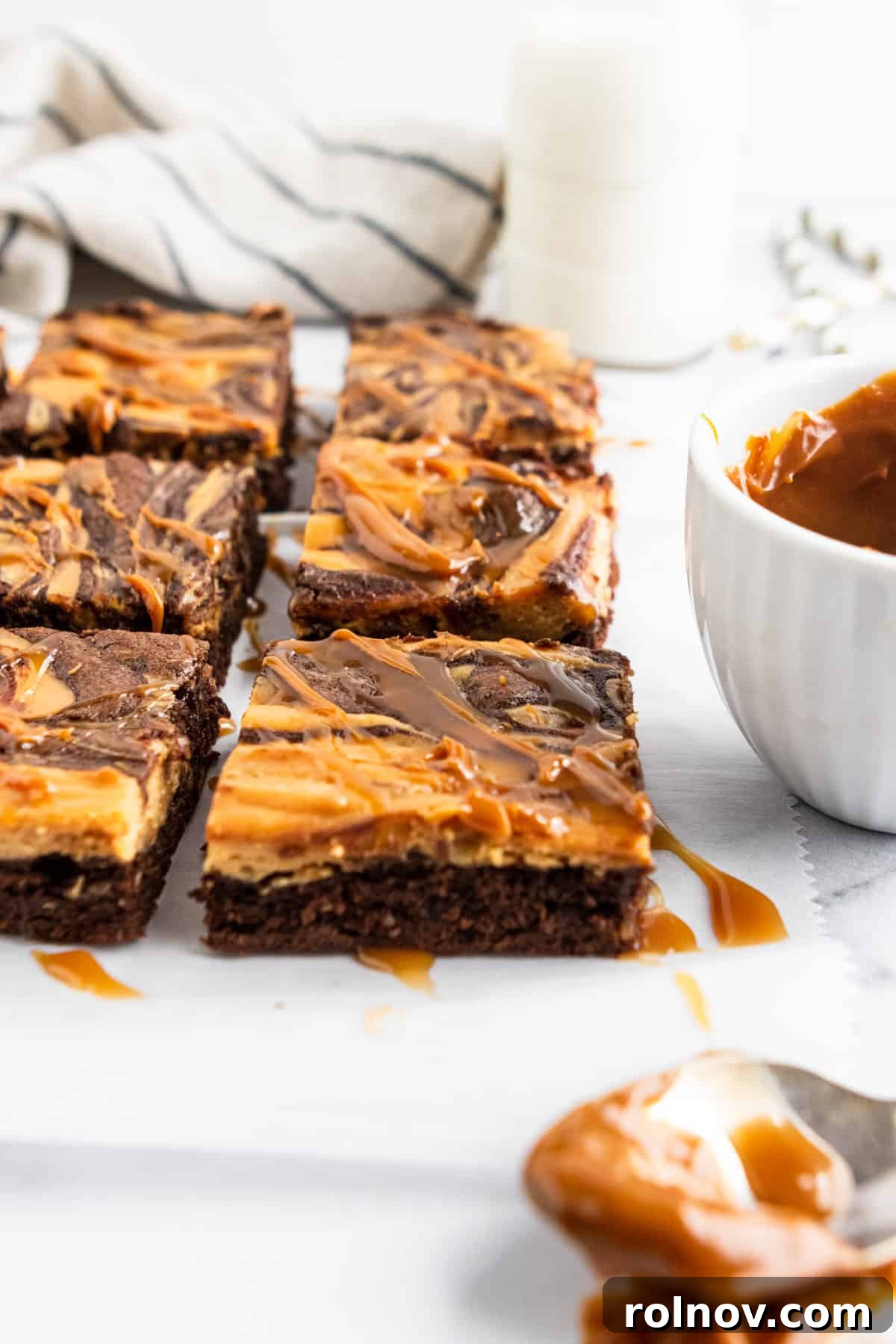 Sliced brownies with drizzle. A side view of several sliced brownies, highlighting the contrasting layers of dark chocolate brownie and light, swirled cheesecake.