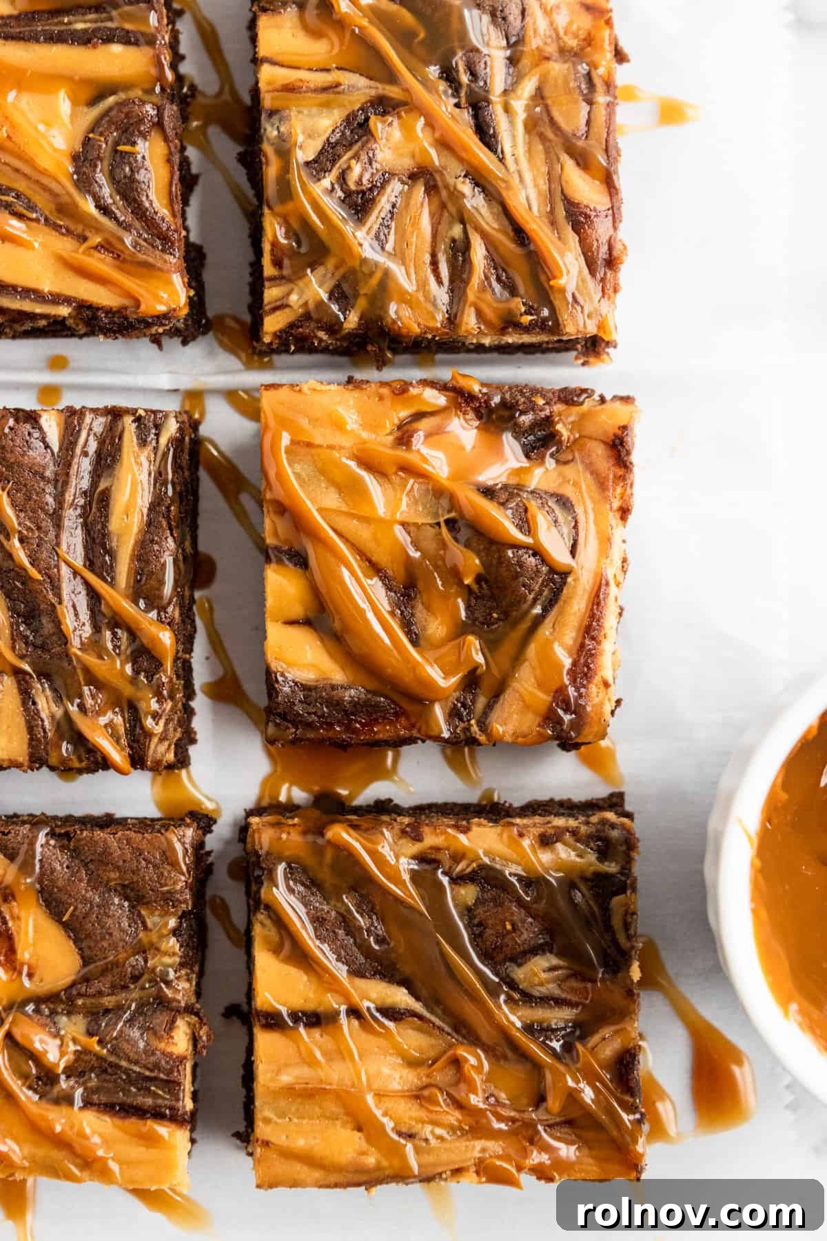 Overhead shot of brownies with dulce de leche drizzle. A beautifully arranged overhead shot of multiple sliced brownies, each topped with an artistic swirl and a golden drizzle of dulce de leche, showcasing their delectable layers.