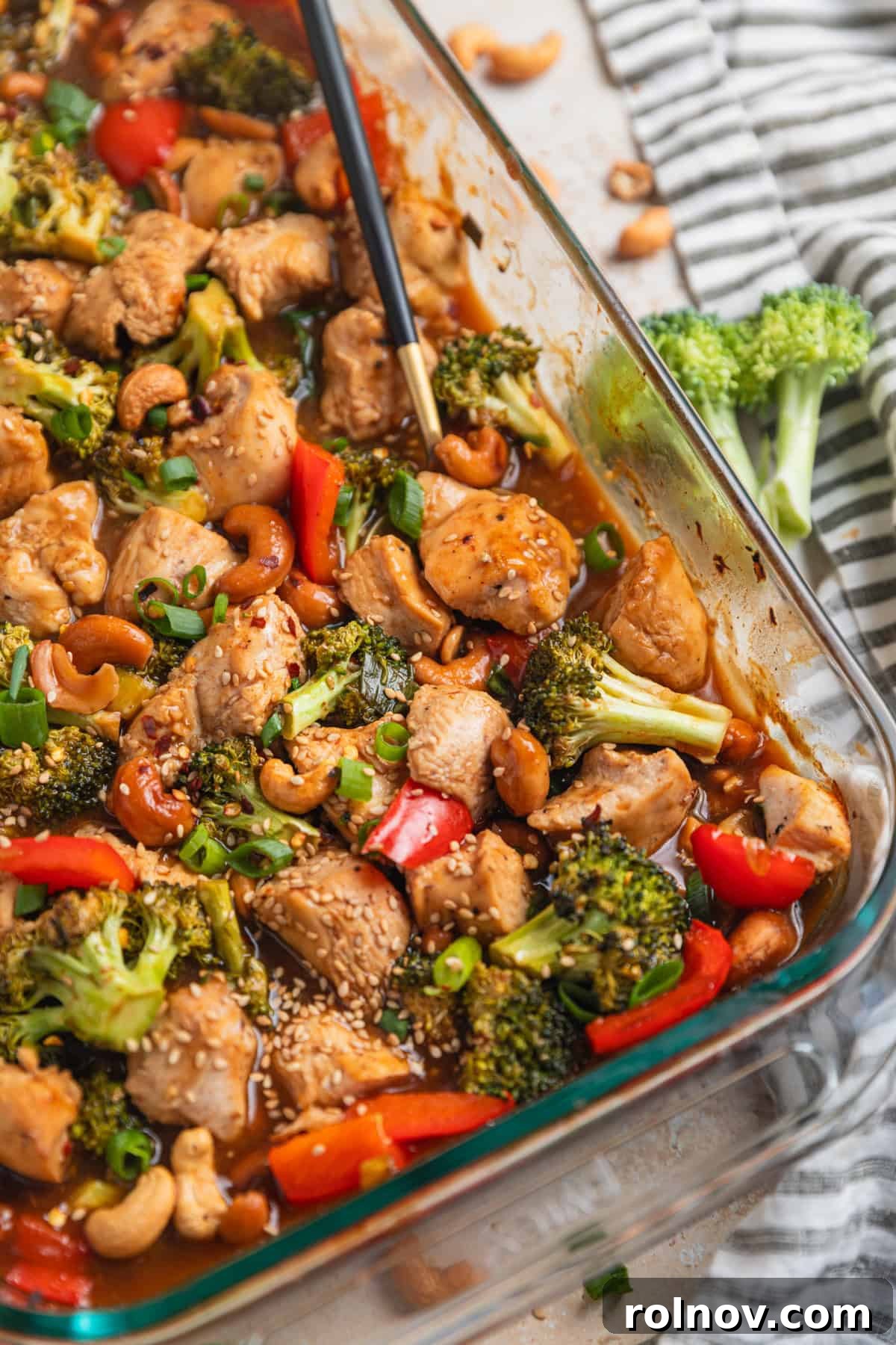 Golden Baked Cashew Chicken 2 Glass baking pan with easy cashew chicken recipe and spoon scooping into it.