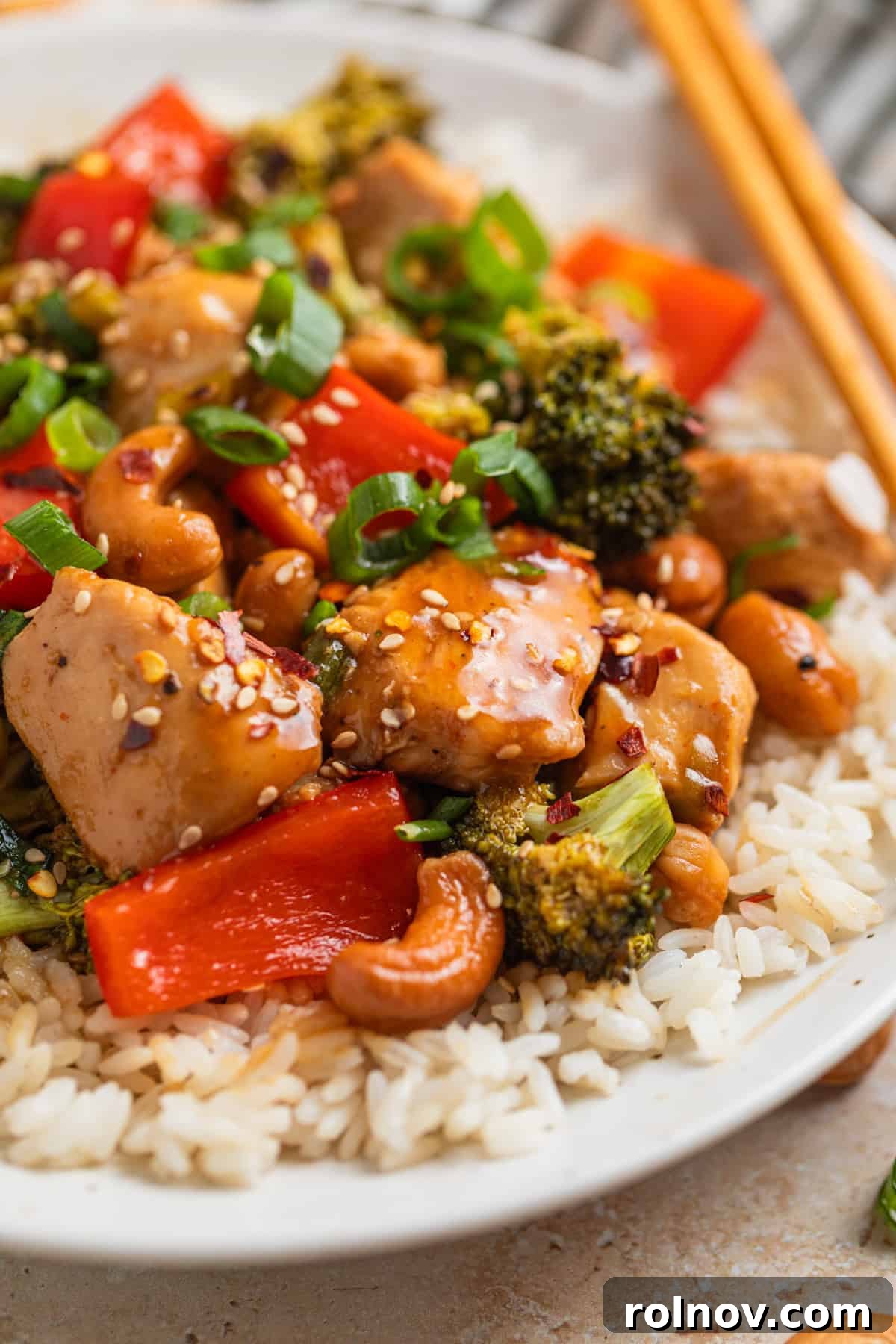 Golden Baked Cashew Chicken 10 Ceramic plate with rice covered in chicken, red bell pepper, broccoli, green onion and sesame seeds.