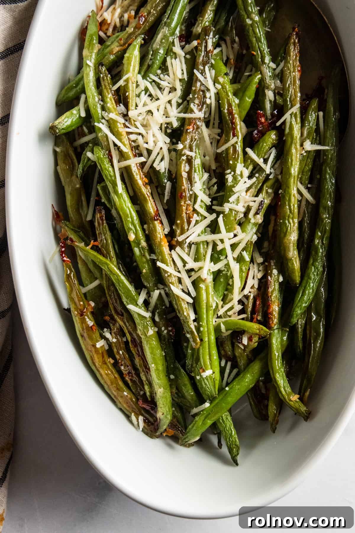 Crispy Roasted Parmesan Green Beans 3 A white serving bowl filled with roasted green beans, glistening with olive oil and parmesan cheese, ready to be served.