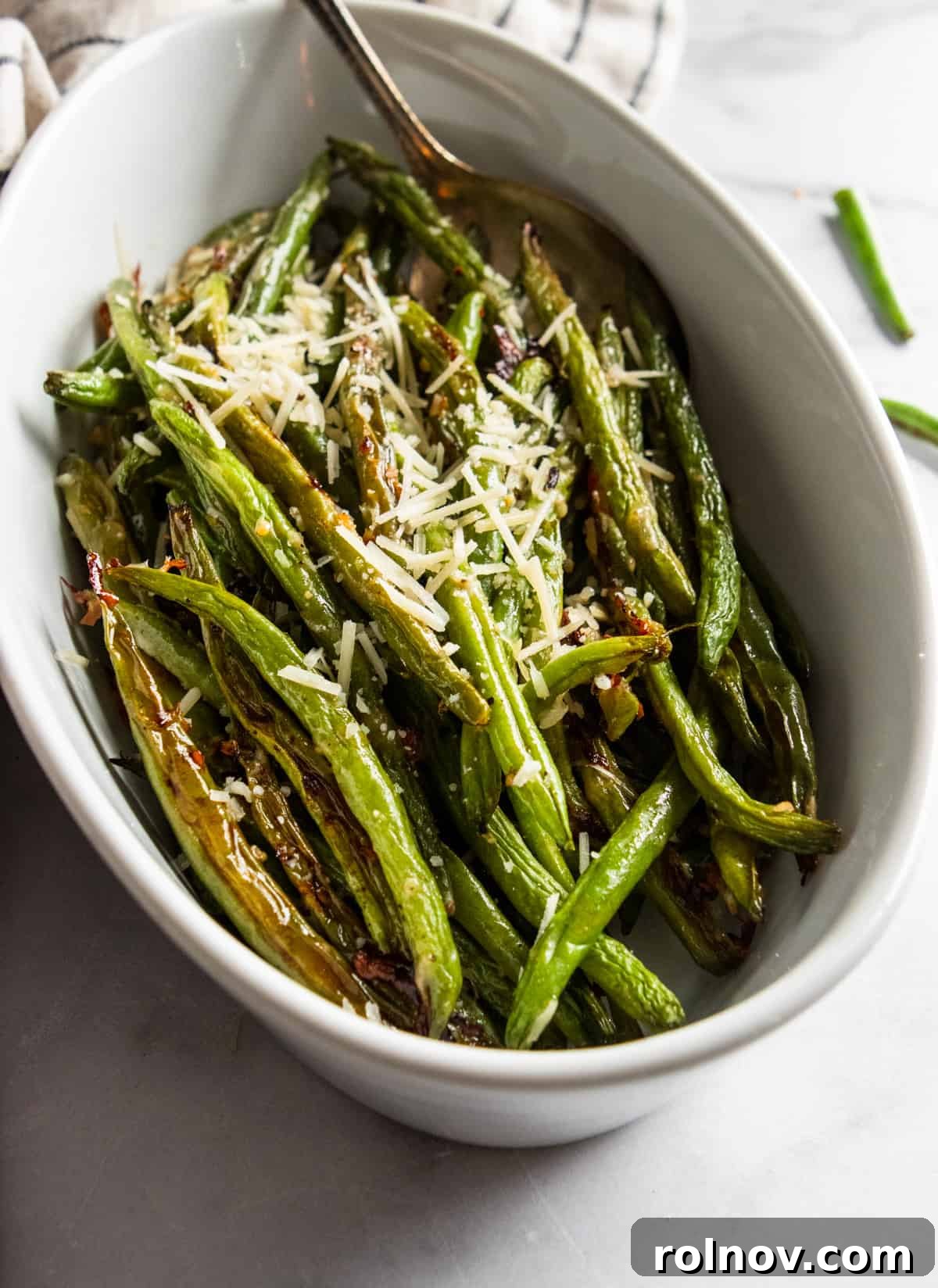 Crispy Roasted Parmesan Green Beans 4 Close-up of roasted green beans in a white serving bowl, sprinkled with fresh Parmesan and herbs.