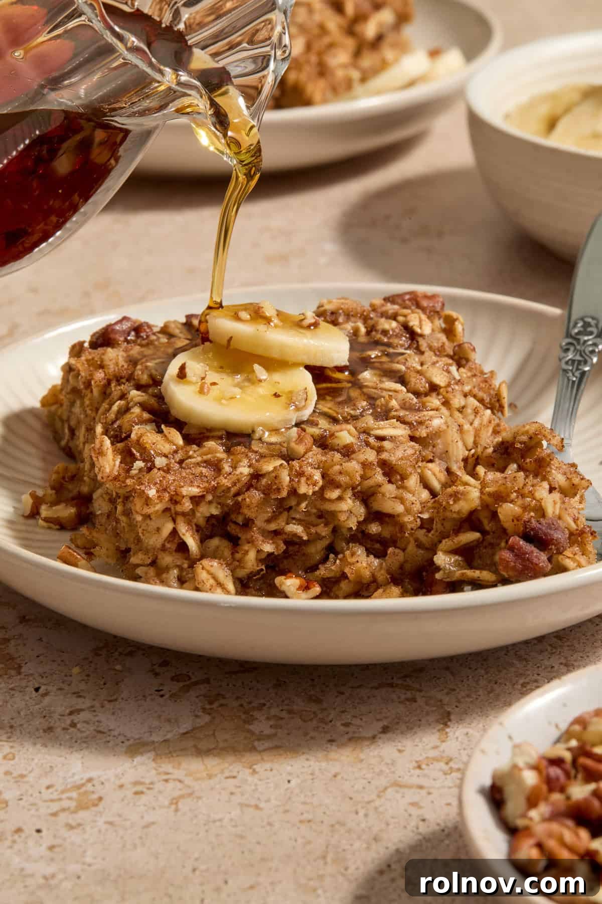 Ultimate Banana Bread Baked Oatmeal 2 A warm slice of Banana Bread Baked Oatmeal drizzled with maple syrup on a white plate, ready to be enjoyed.
