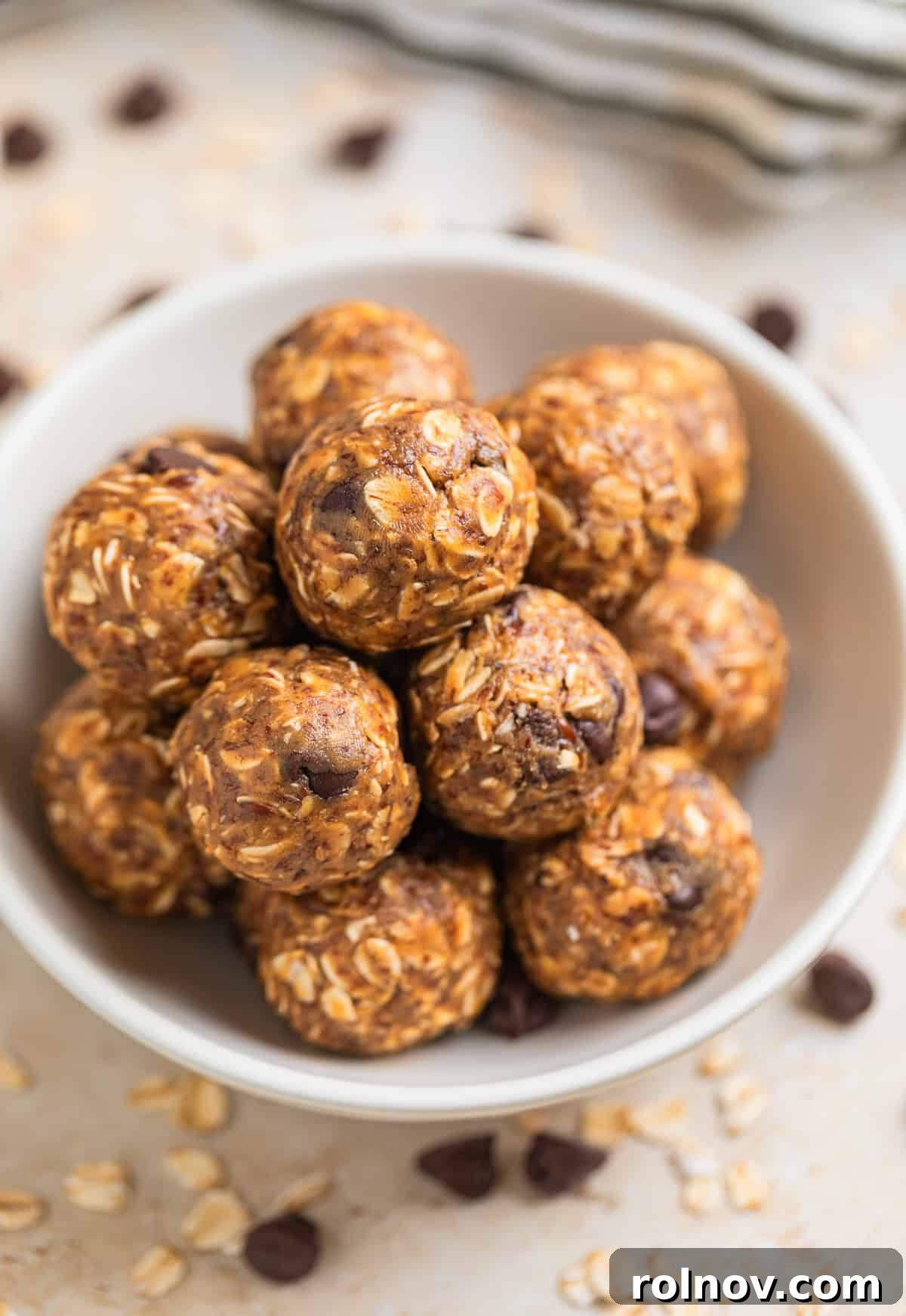 Peanut Butter Oatmeal Energy Bites 2 A white dish filled with golden-brown no-bake peanut butter oatmeal balls, garnished with scattered rolled oats and chocolate chips.