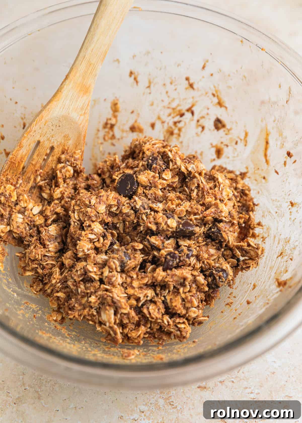 Peanut Butter Oatmeal Energy Bites 6 Glass bowl containing the oat mixture, with chocolate chips stirred in by a wooden spoon.