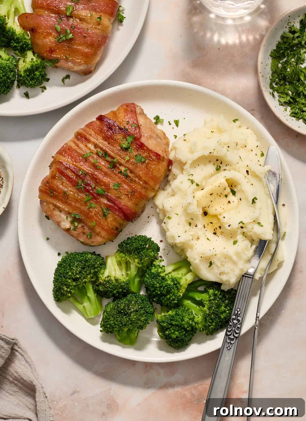 Sweet and Savory Maple Bacon Pork Chops 2 Overhead view of a plate with a crispy bacon-wrapped pork chop, vibrant green broccoli florets, and creamy mashed potatoes.